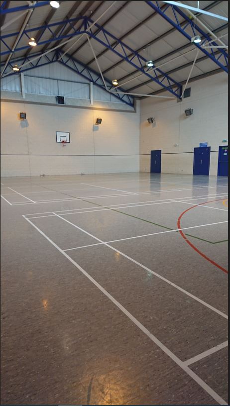 The games hall features floor markings designated for badminton and basketball, along with a basketball hoop positioned on the end wall.