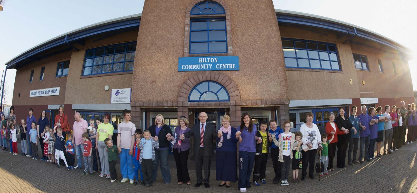 A contemporary building surrounded by a multitude of people gathered around its periphery.