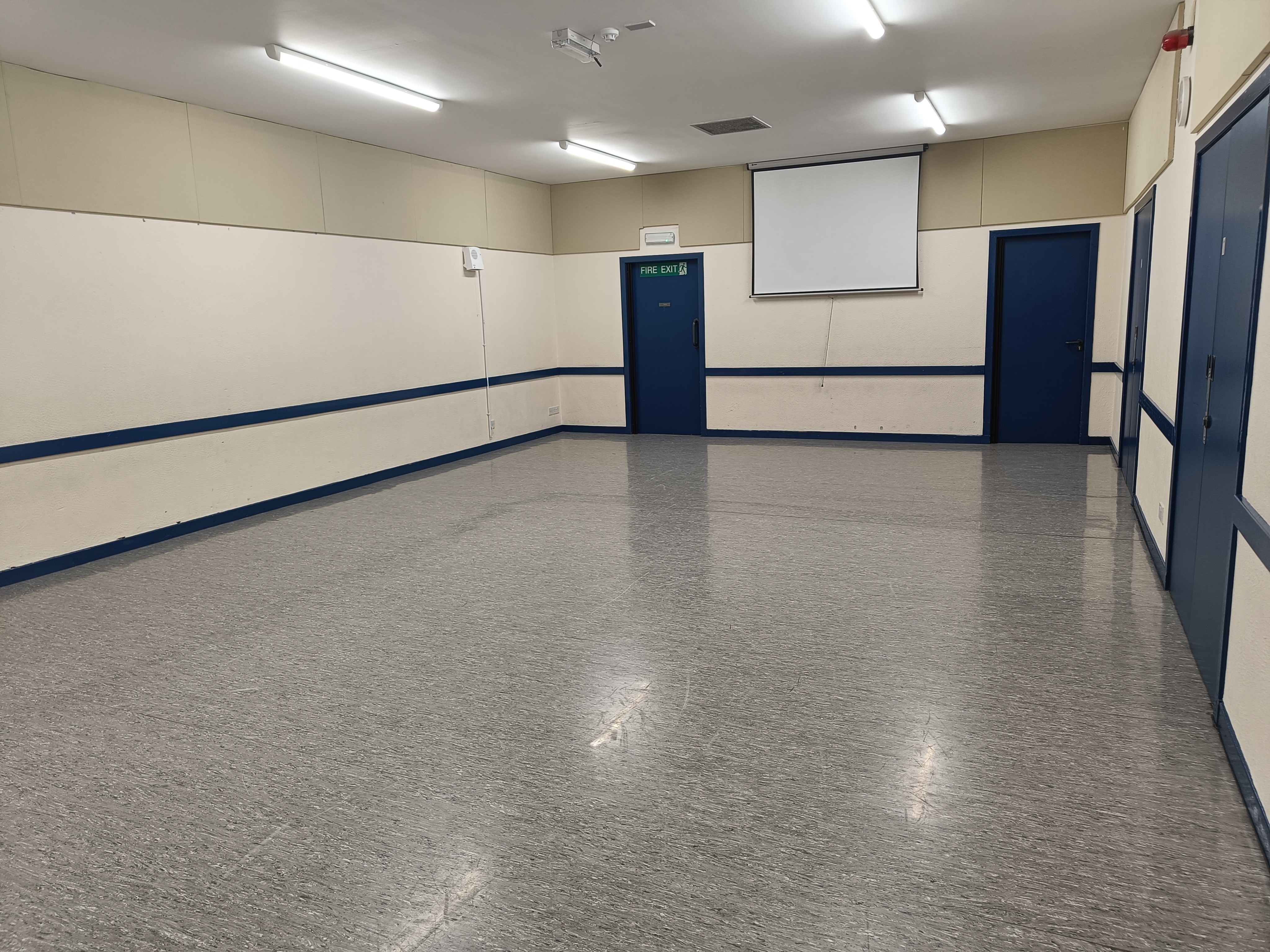 A bright and spacious room featuring linoleum flooring and a white screen on the far wall.