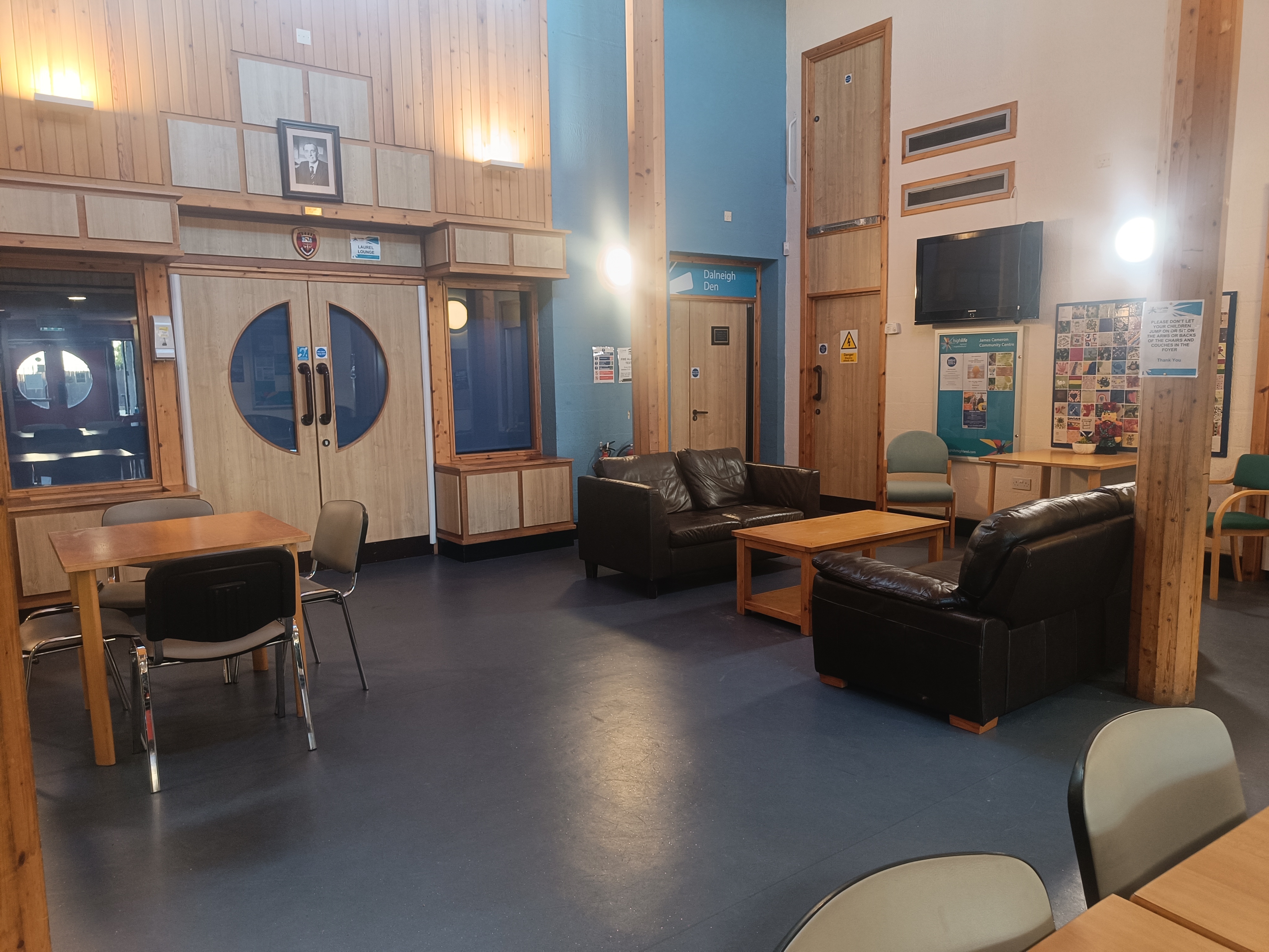 A spacious and well-lit open area featuring comfortable sofas, tables, chairs, and multiple entrance / exit doors.