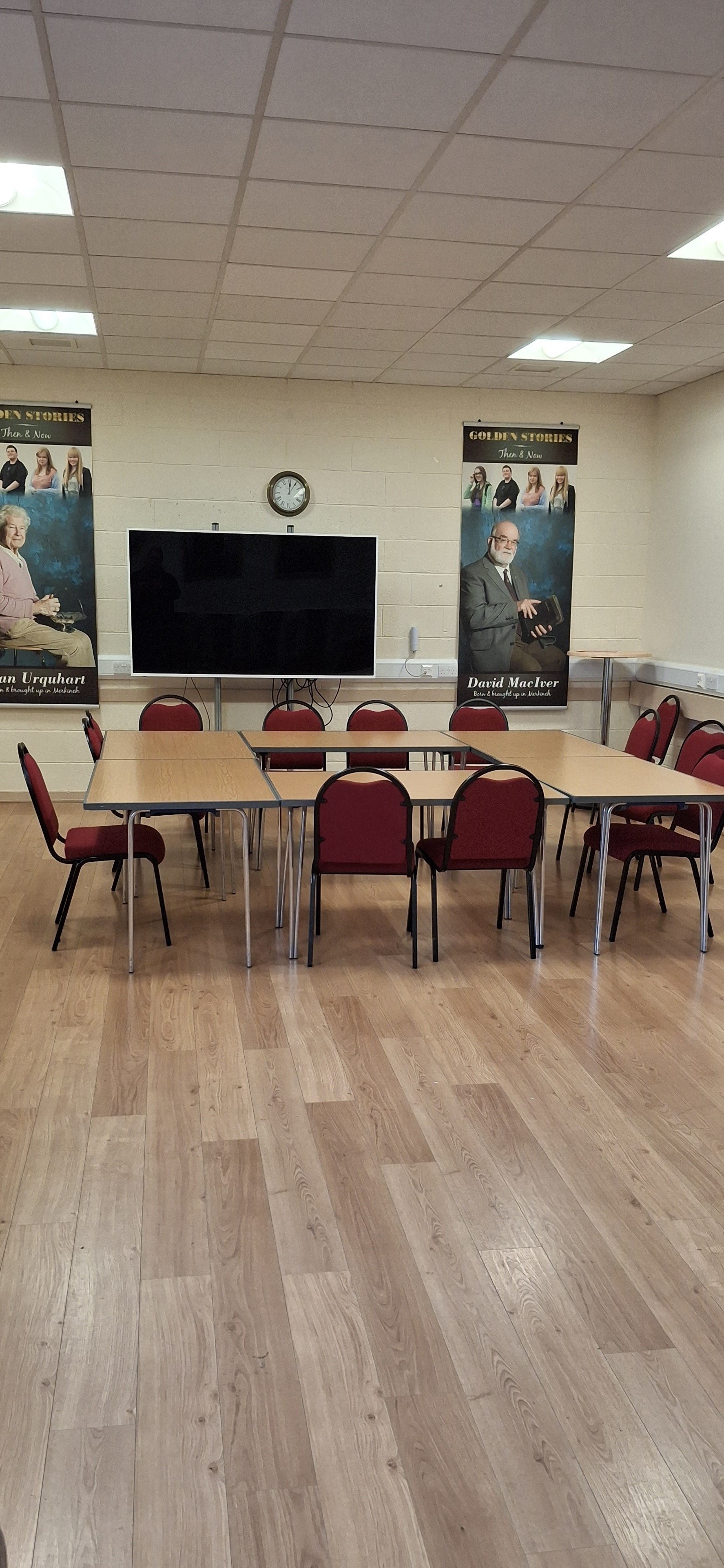 The room is adorned with linoleum flooring and features a wall-mounted television, complemented by a meeting table encircled by chairs.