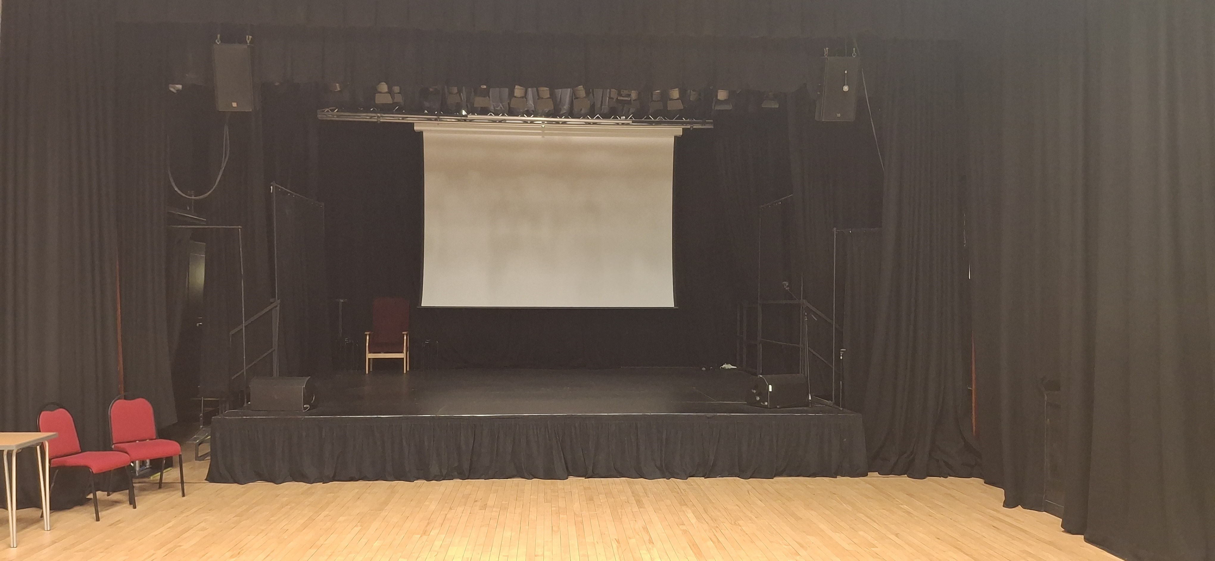 The hall draped in black curtains with a stage equipped with a retractable white screen, perfectly suited for presentations.