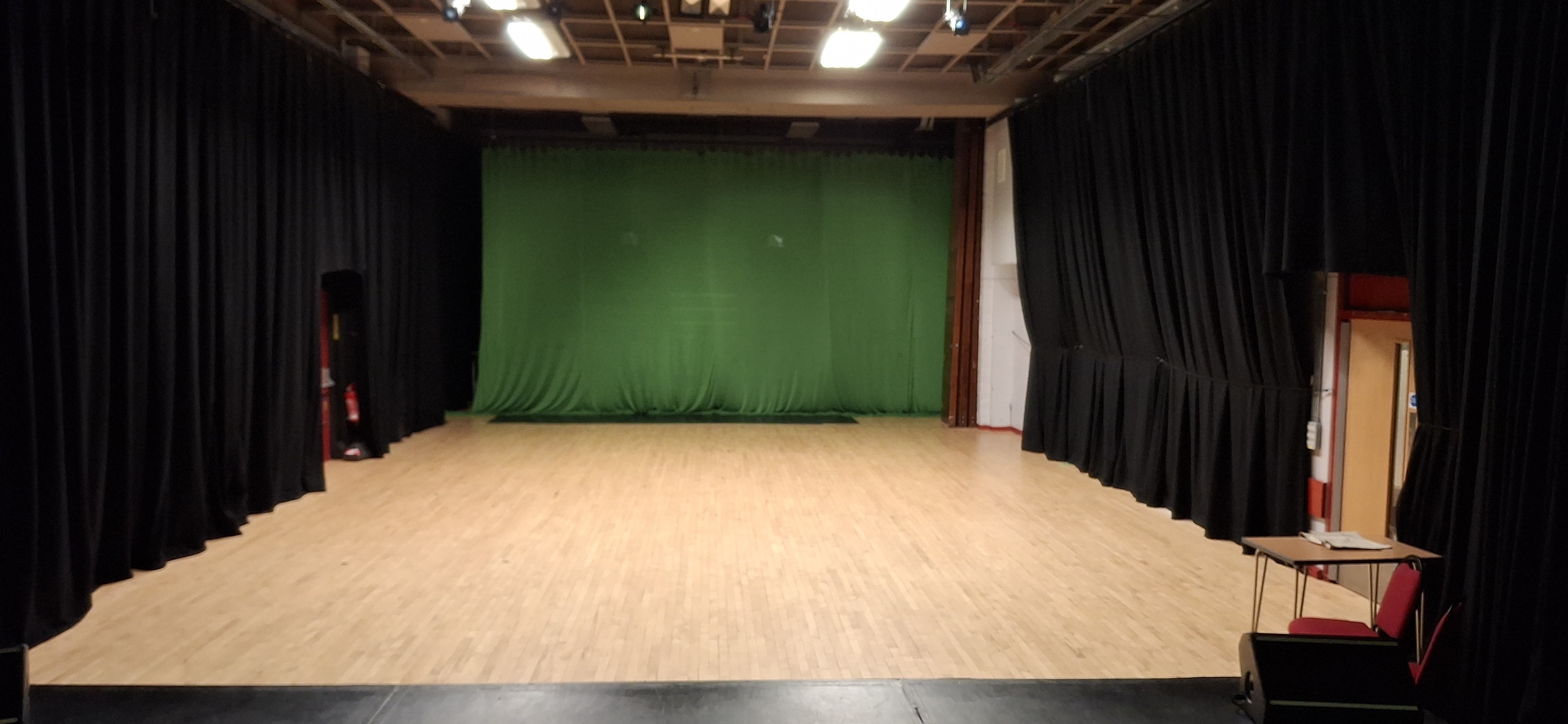 A spacious hall adorned with black curtains, featuring a screened-off stage.