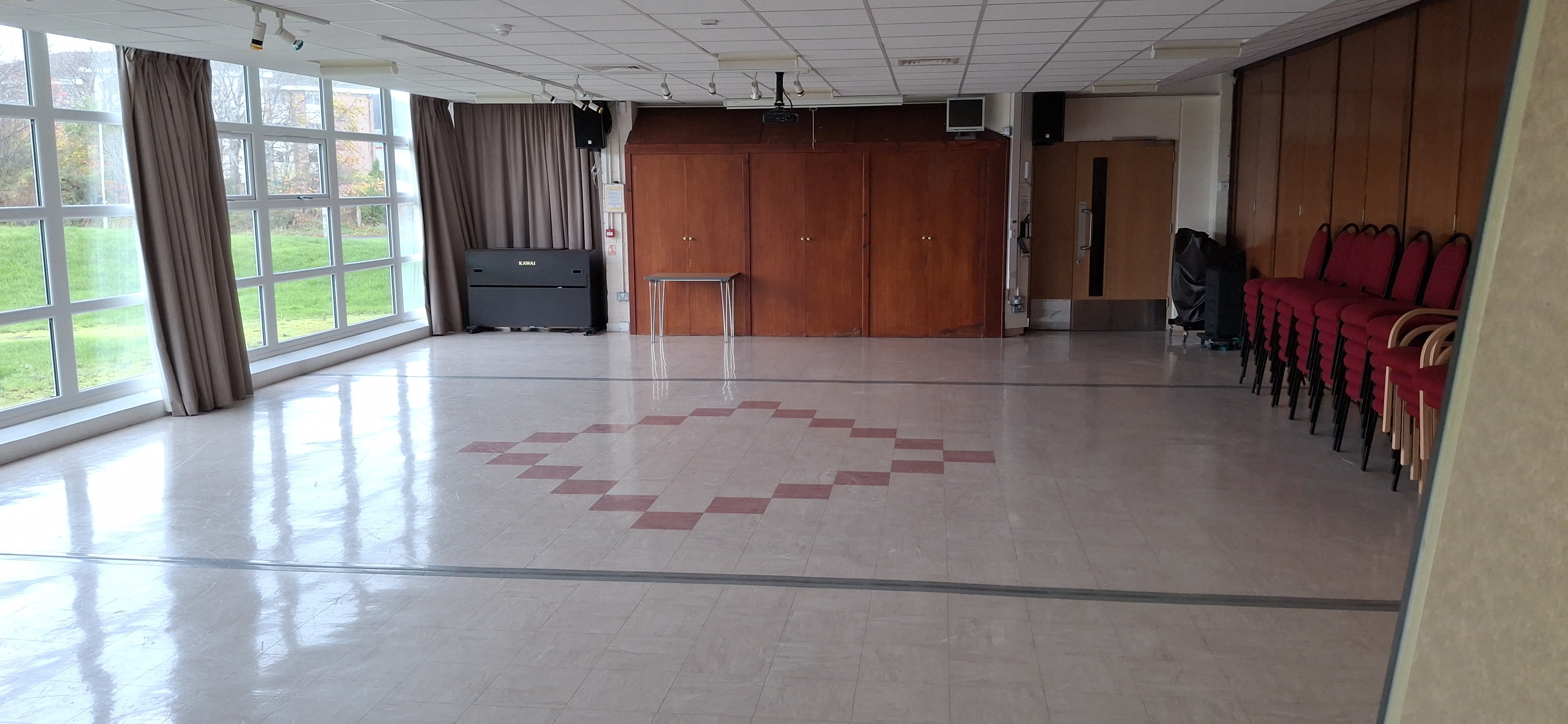 A spacious room bathed in natural light, enhanced by floor-to-ceiling windows and adorned with patterned linoleum flooring.