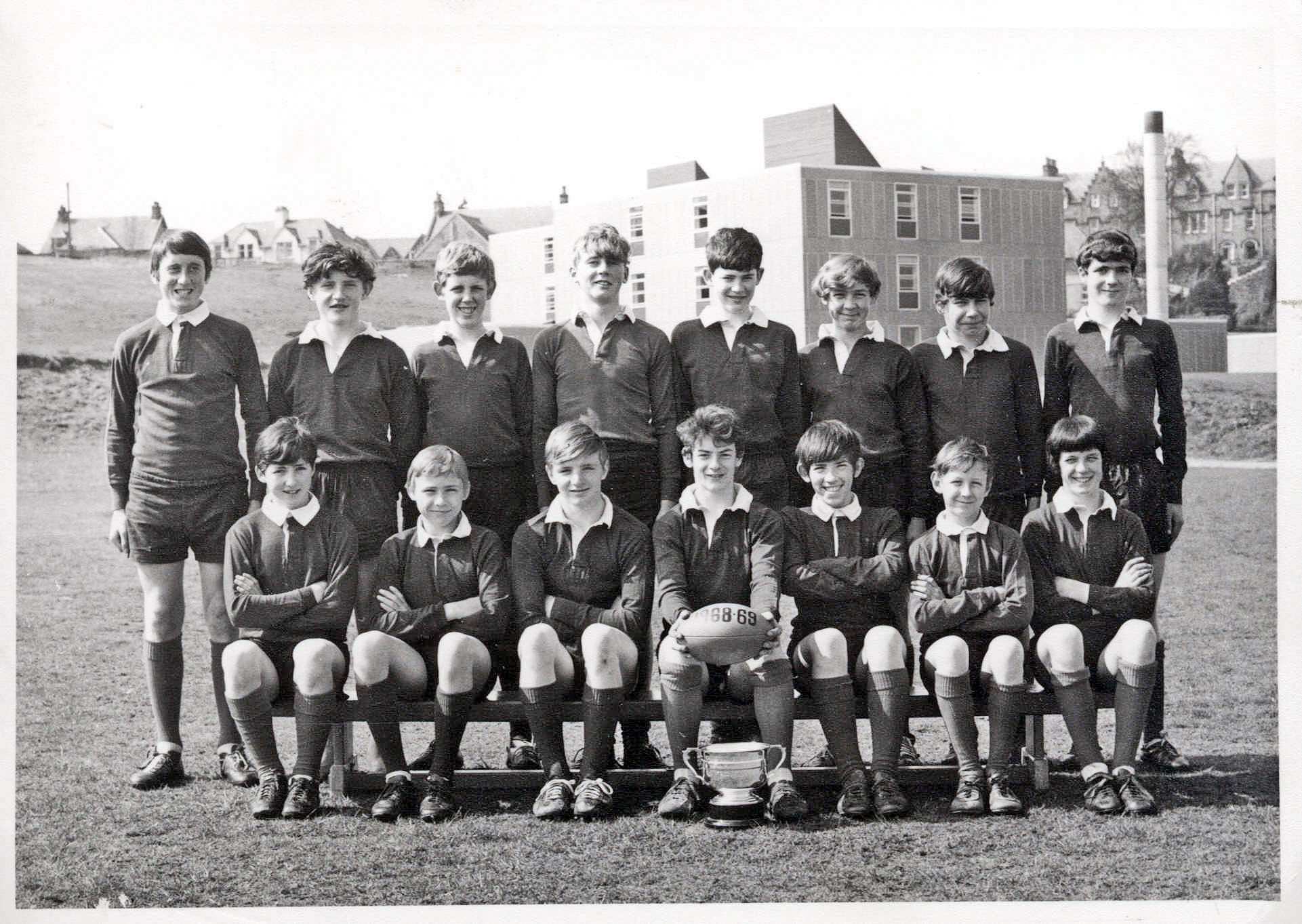 Black and white team photograph of Millburn Secondary School's senior rugby squad for 1968–69, posed on a sports field with the Bon-Accord Cup trophy.