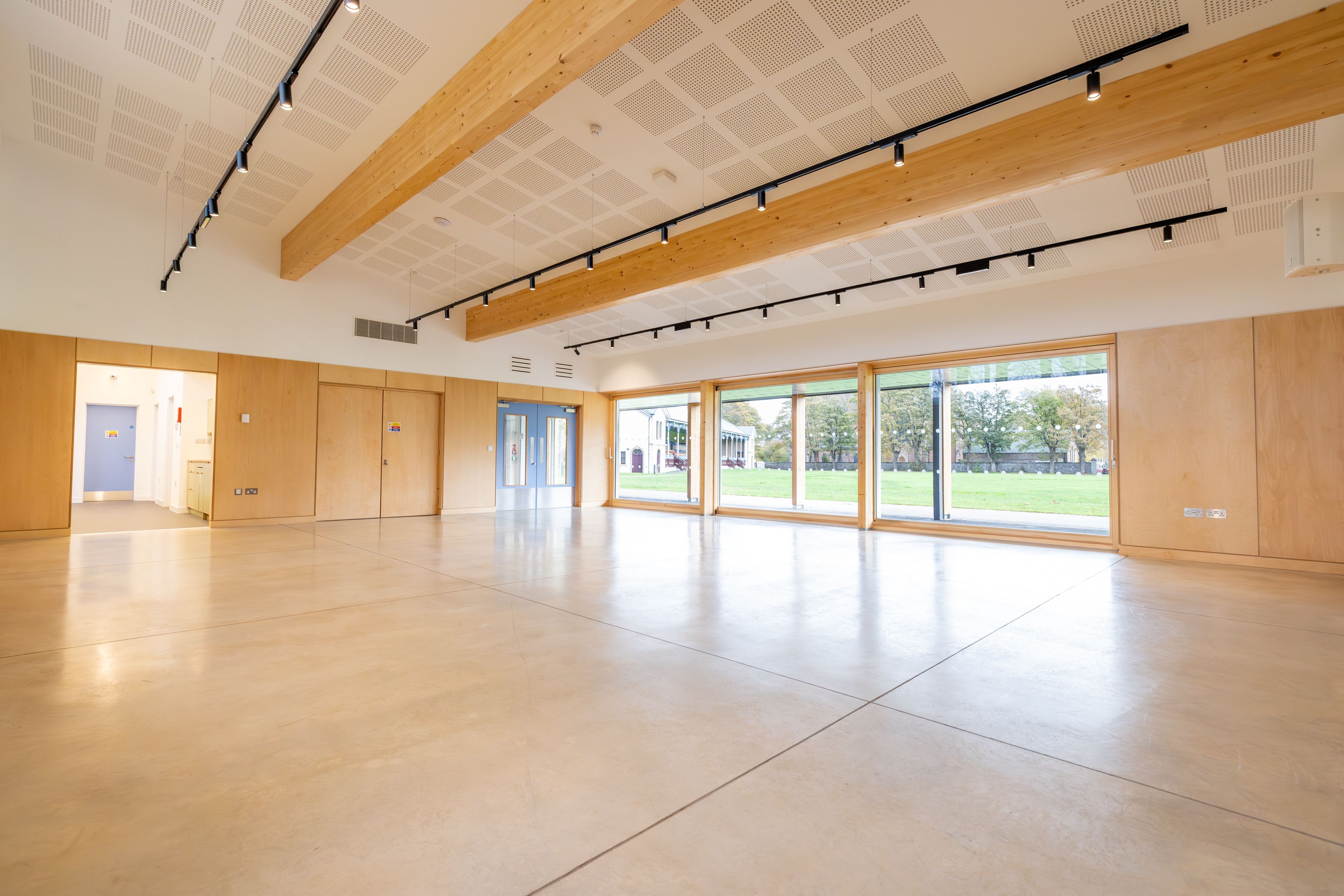 The room is spacious and features floor-to-ceiling windows, along with sliding doors that open to an adjacent grass park.