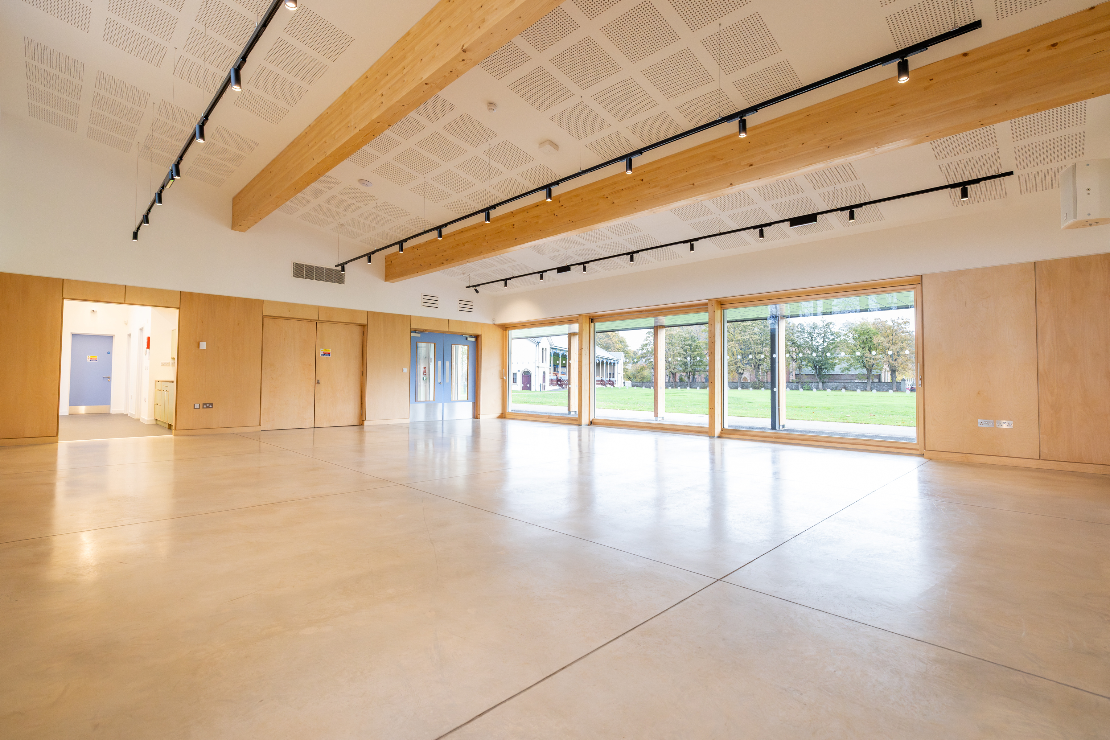 The room is spacious and features floor-to-ceiling windows, along with sliding doors that open to an adjacent grass park.