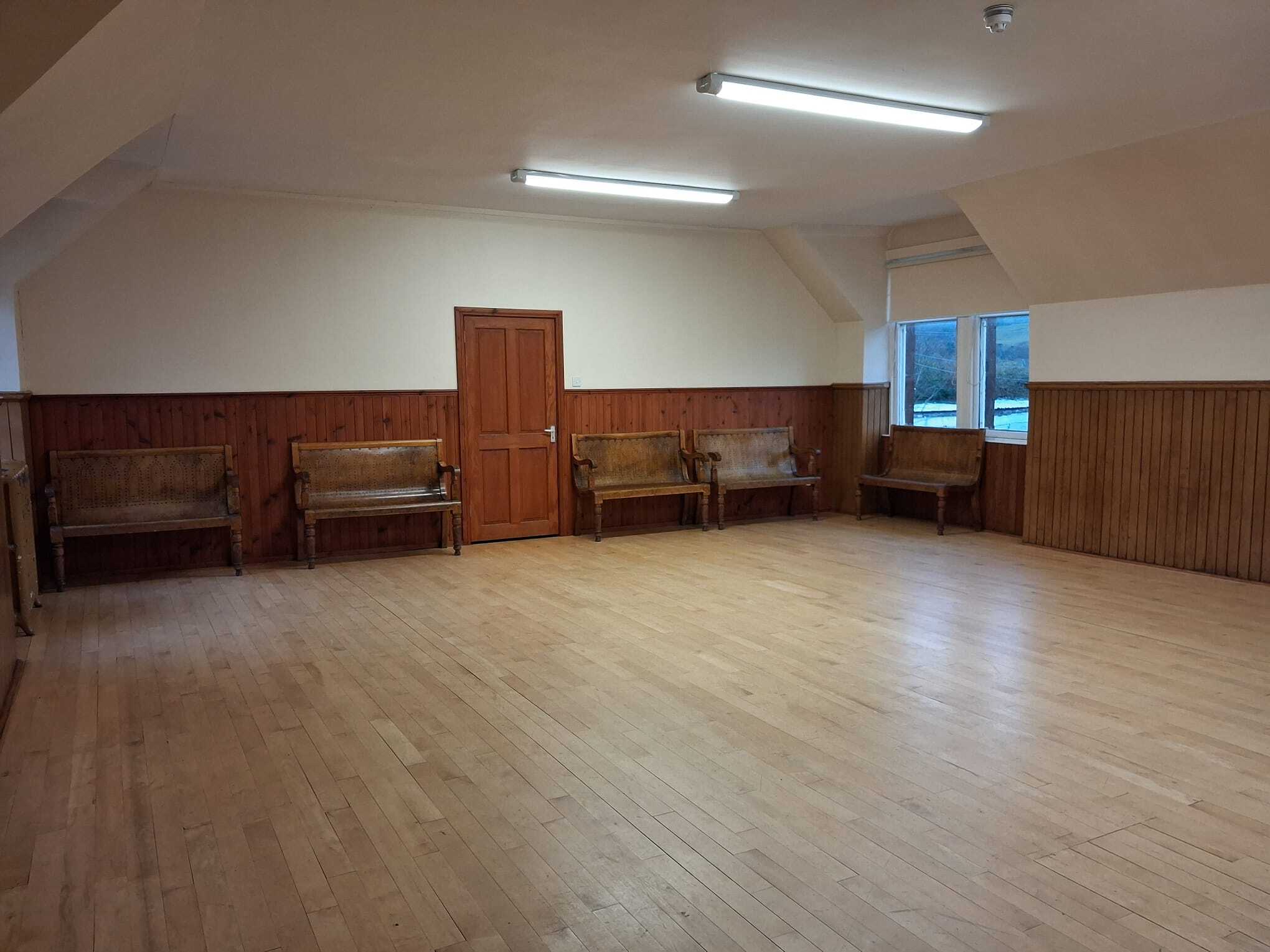 The Ceilidh room is an expansive hall featuring hardwood flooring and abundant natural light that pours in through large windows.