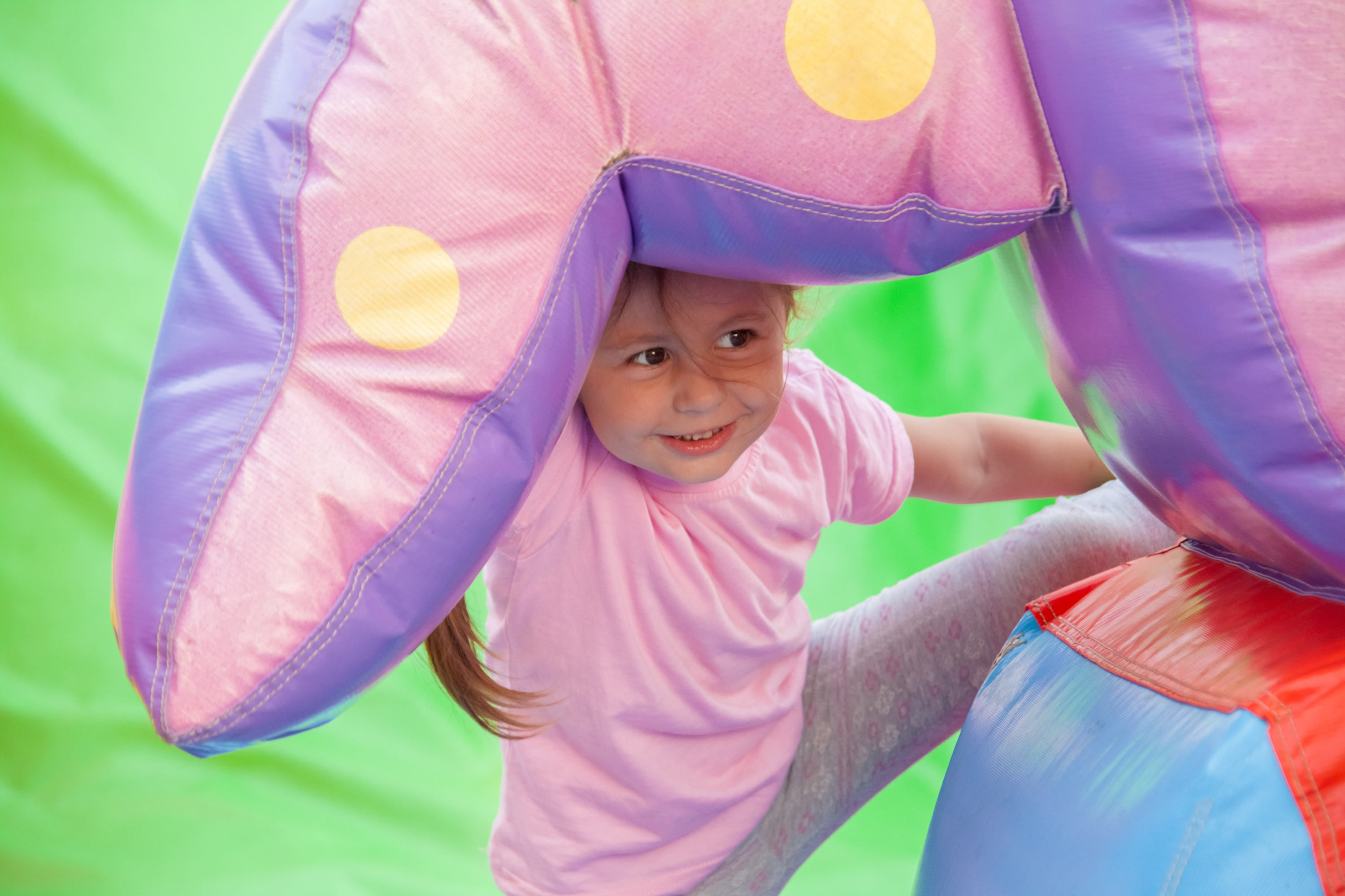 Young girl wearing pink t-shirt and grey joggers playing in an inflatable castle. Holding onto part of the inflatable and looking to the right of the camera.
