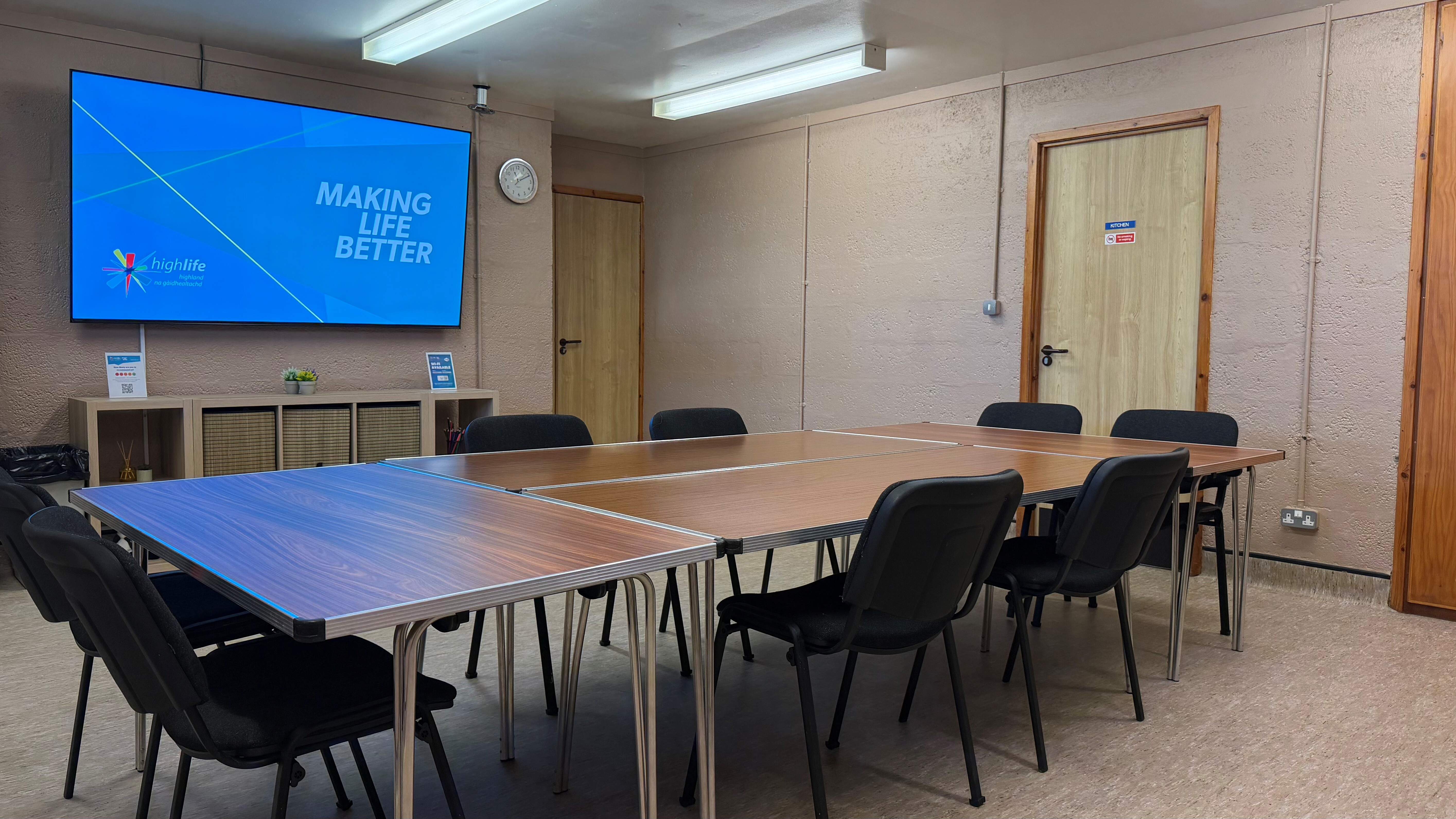 Large tables with chairs in the middle of the room. Large wall-mounted TV for presenting.