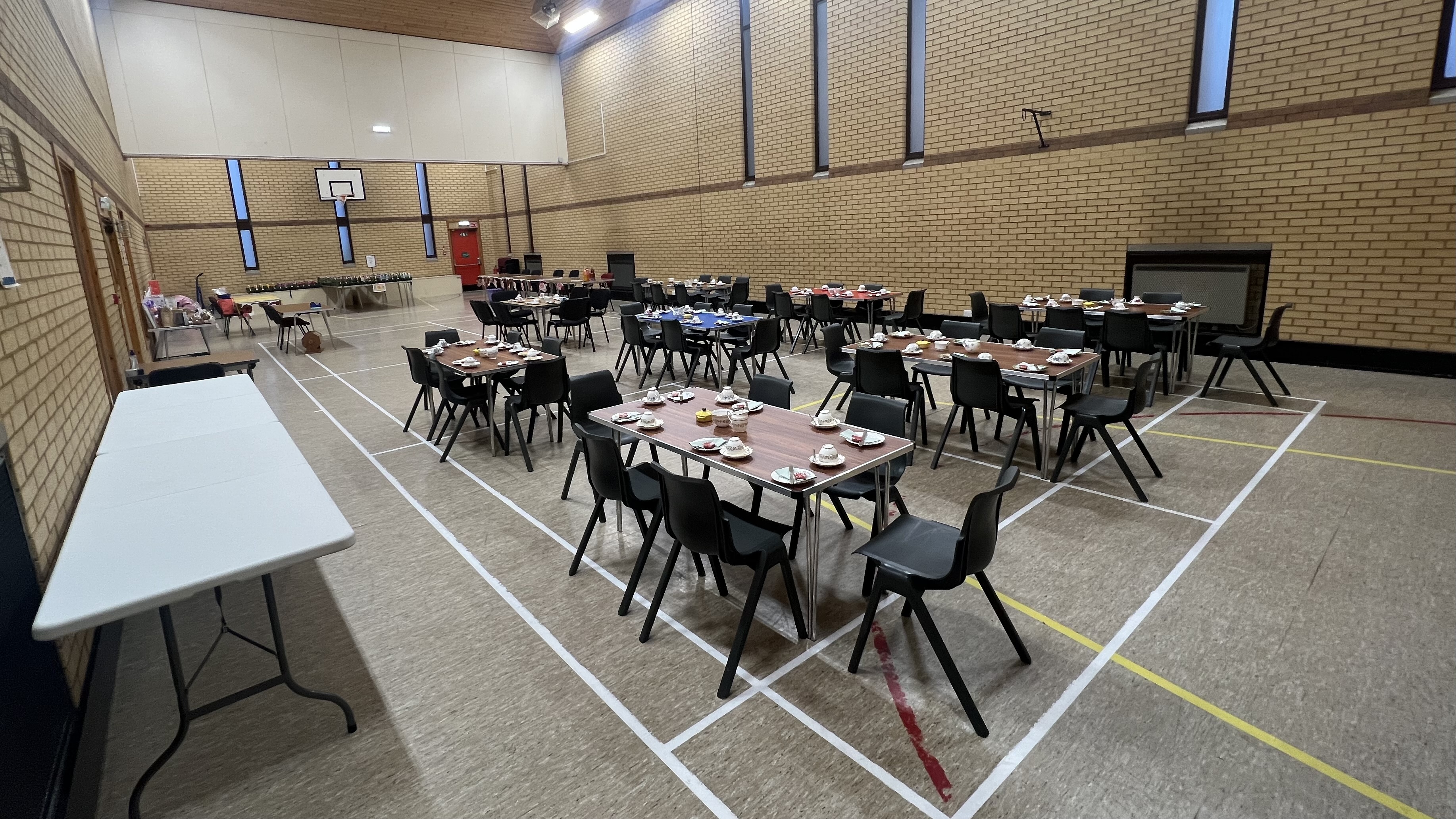 Tables set for a coffee morning inside a sports hall, with chairs and refreshments laid out.