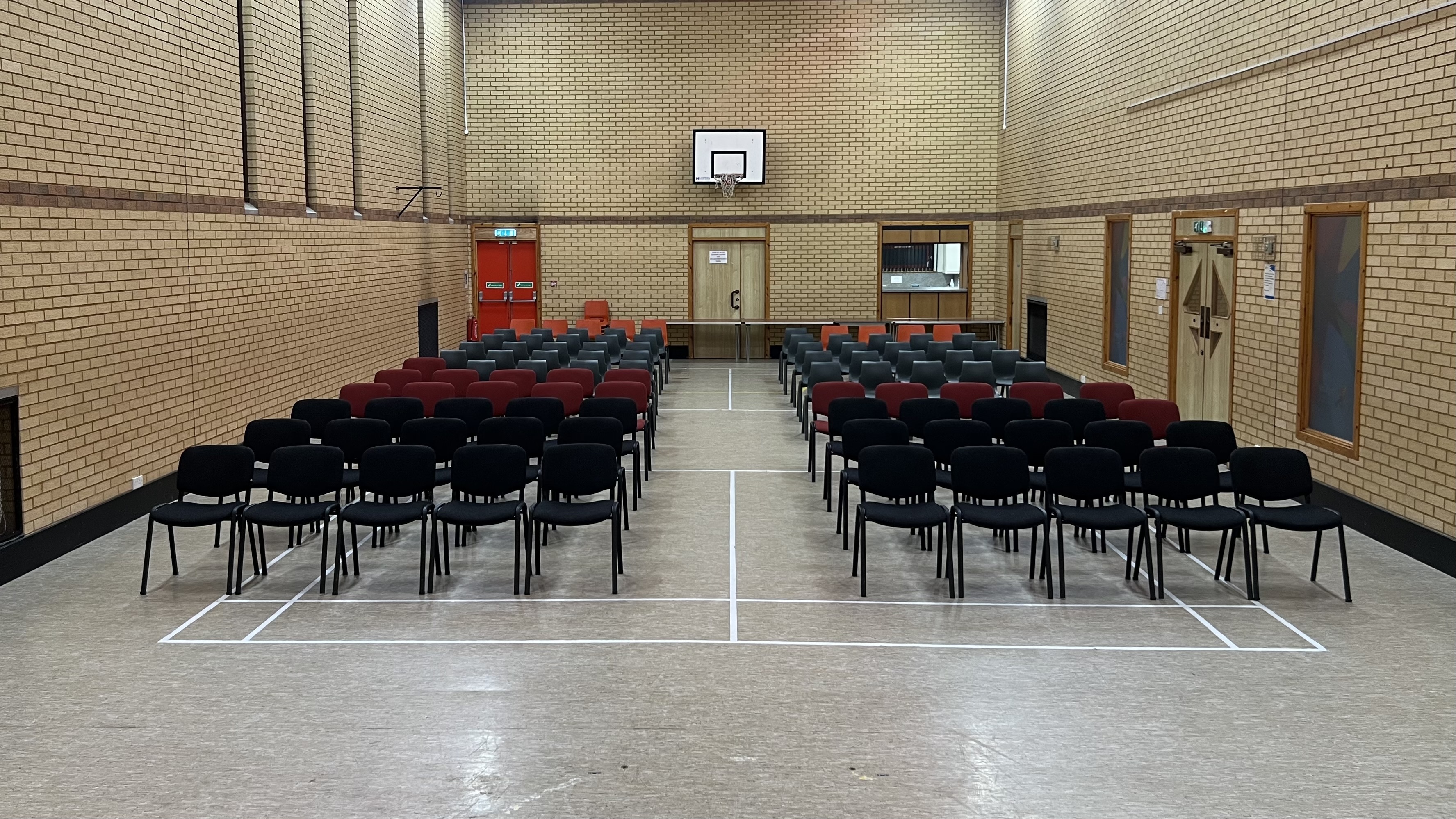 Rows of black and red chairs set up in a sports hall facing a basketball hoop.