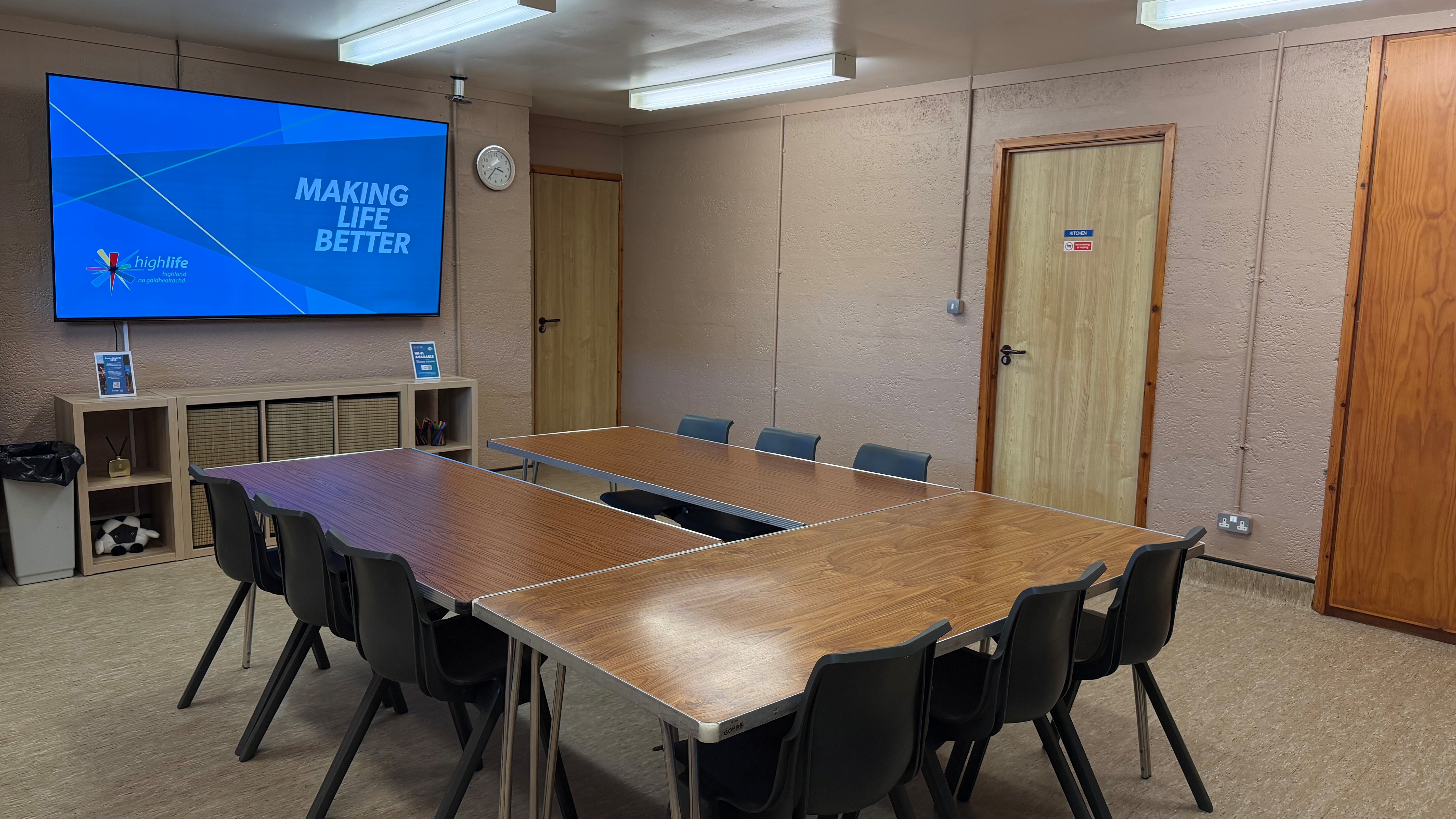 King Duncan's Room set up for a meeting, with tables arranged in a U-shape surrounded by black chairs, facing a wall-mounted screen displaying High Life Highland's 'Making Life Better' branding.