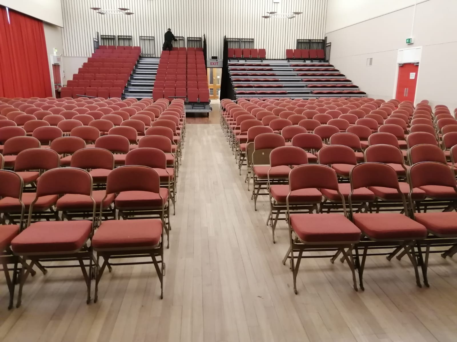 A hall featuring retractable seating at the back of the room, along with additional seating arranged in front of a stage.