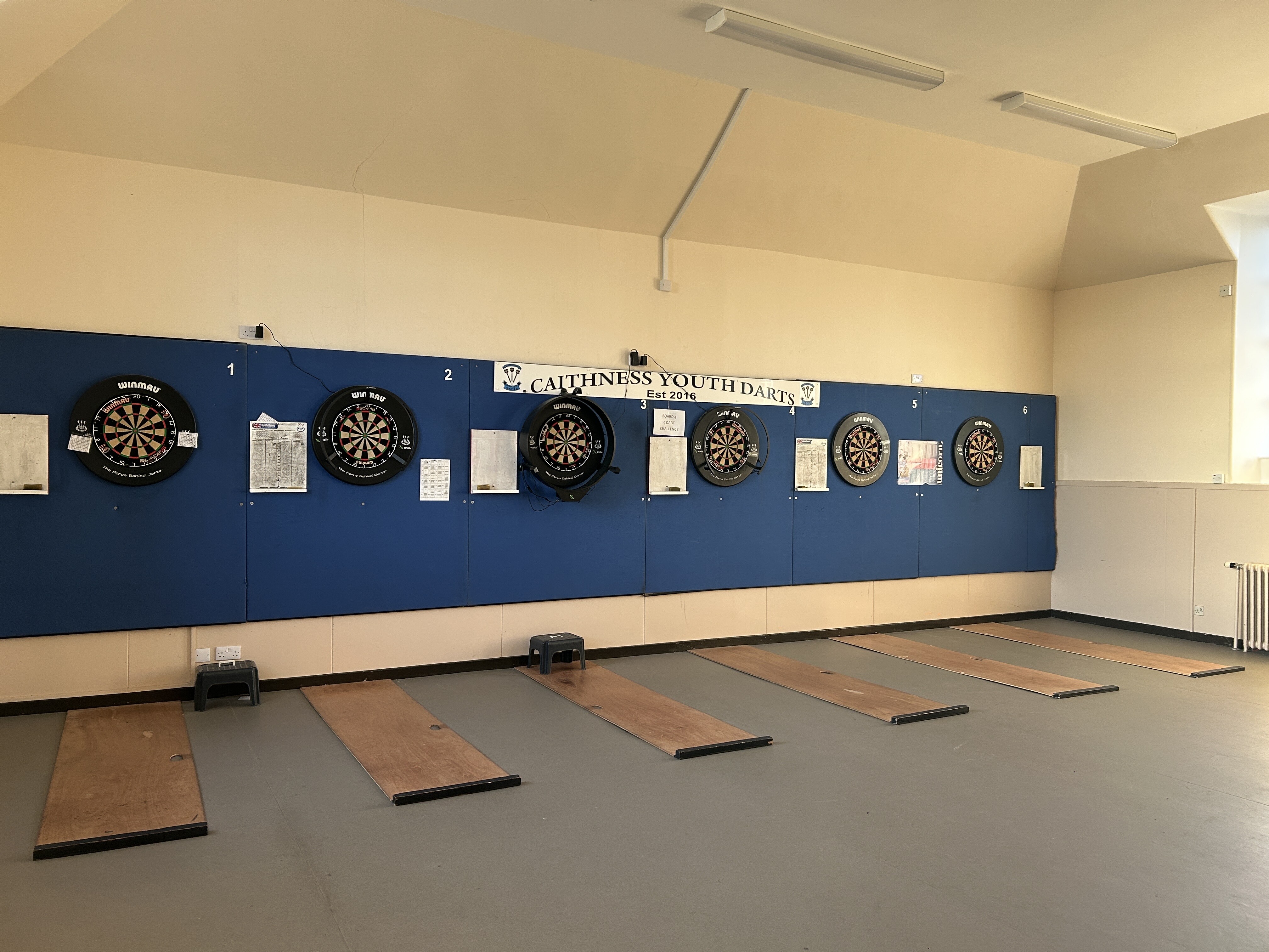Room equipped with 6 dart boards, with mats in front of each board.