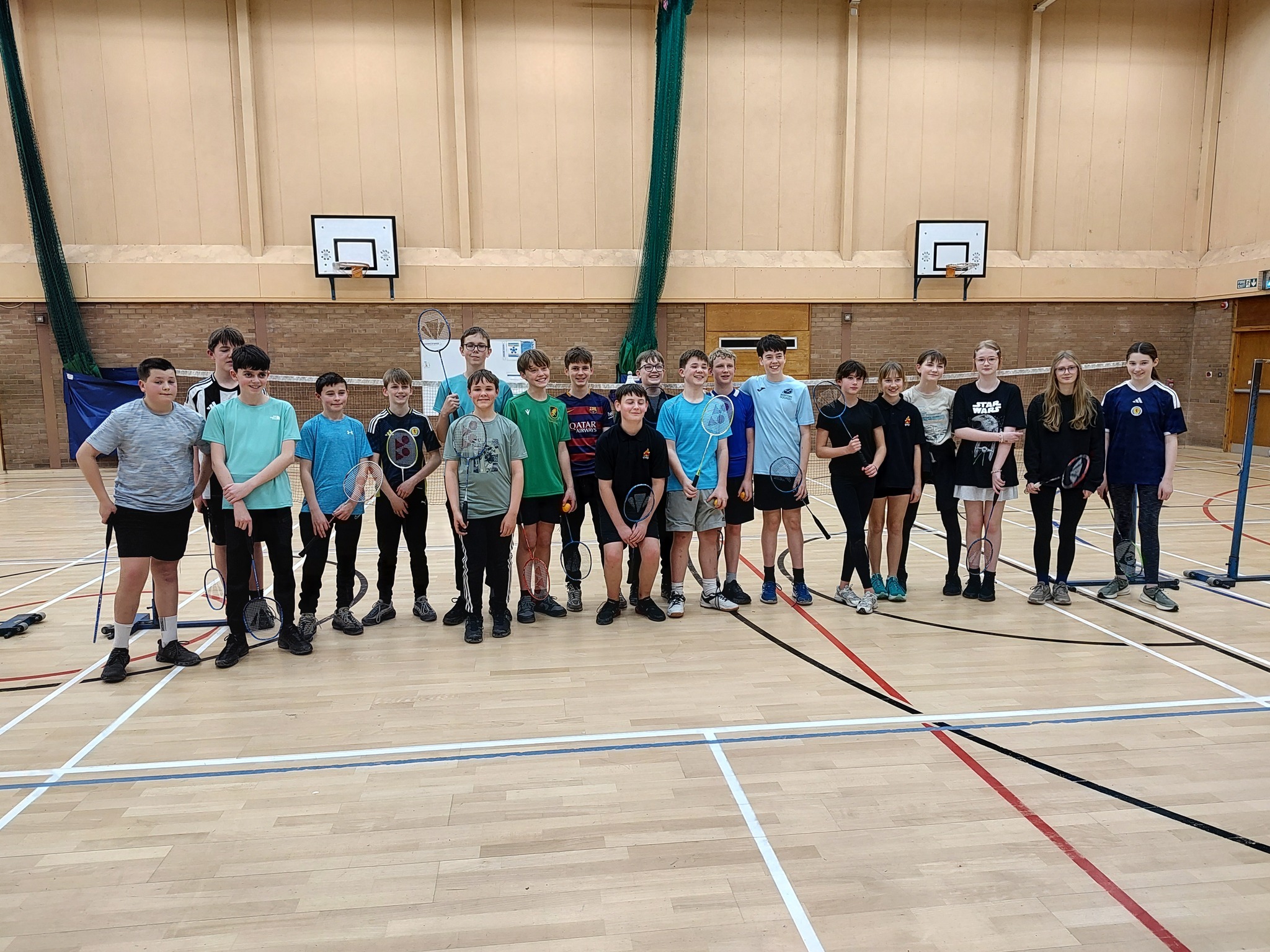 A group of children holding racquets, standing in a row in a sports hall.