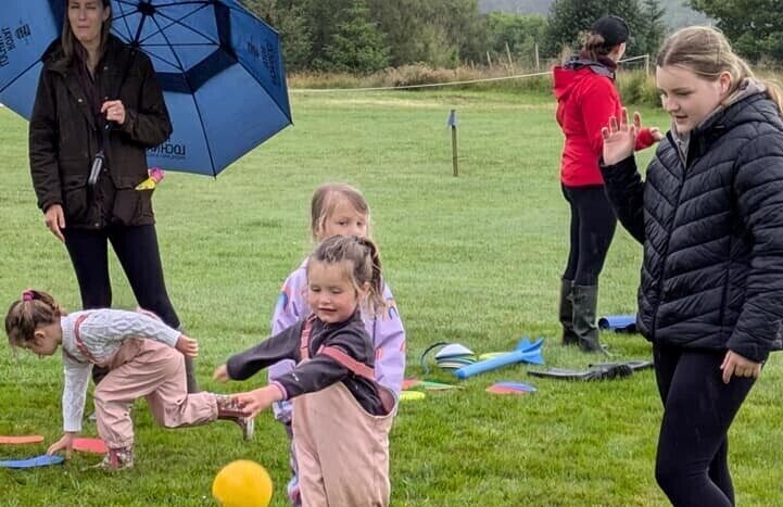 3 very young children in a field with cones and balls and 3 volunteers.