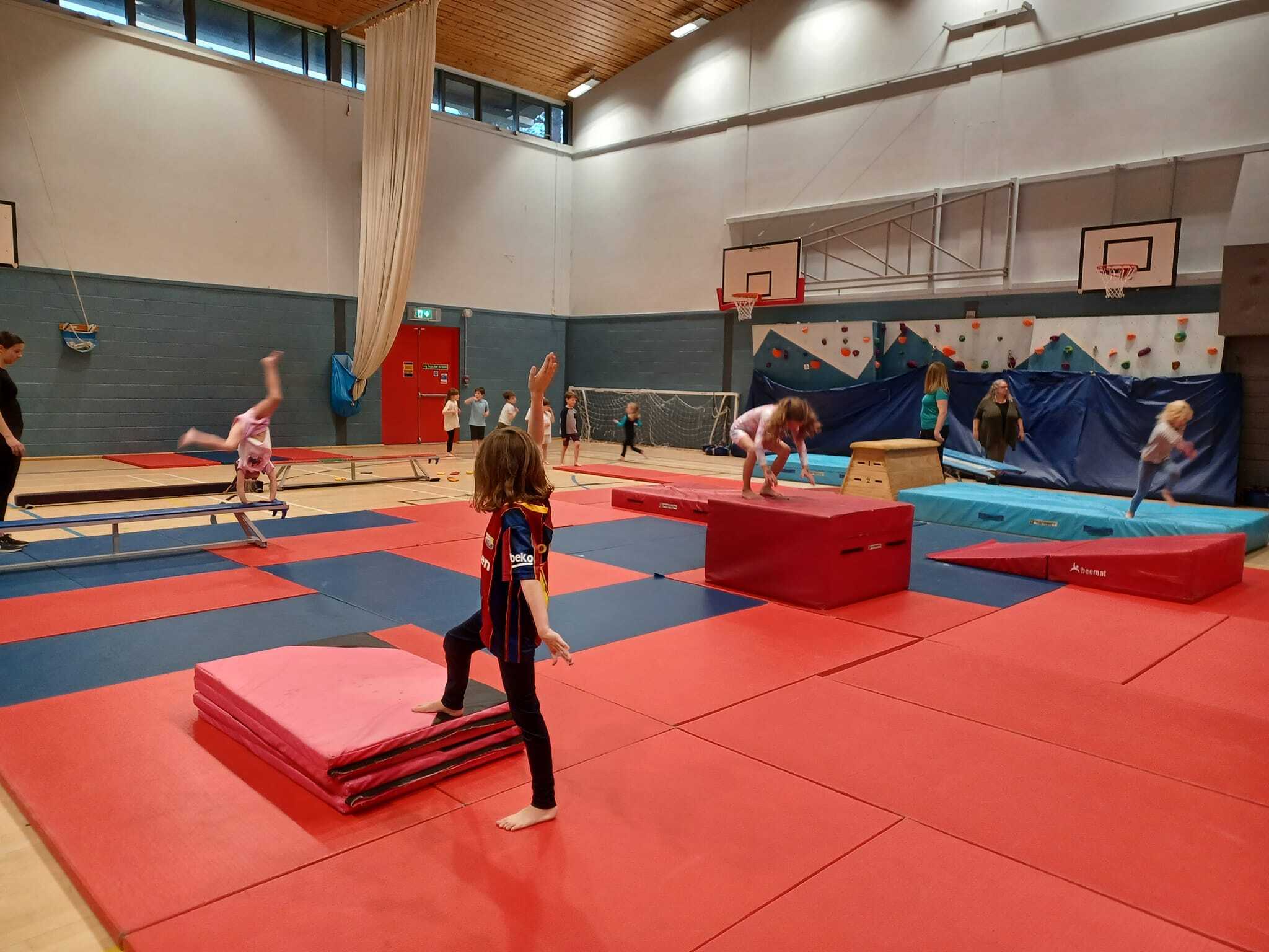 Young children engaged in simple gymnastics on mats and beam in a large gym hall in Grantown.