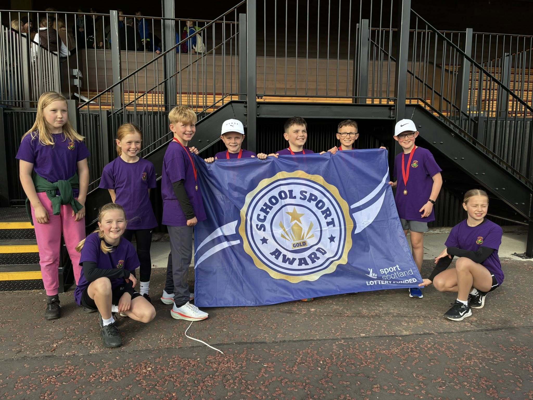 A group of primary school children holding a sportscotland School Sport Award Gold flag.