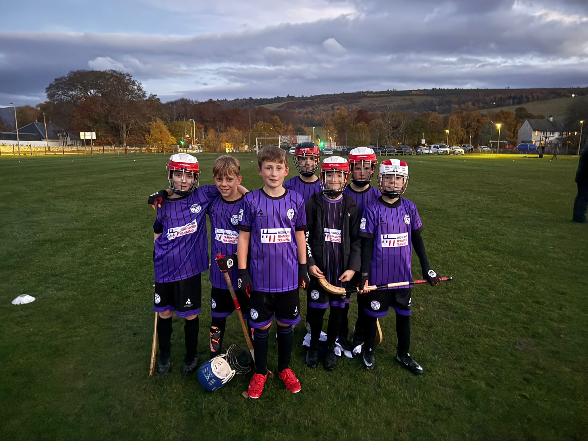Six boys in purple strips pose with shinty camans, and four in shinty helmets.