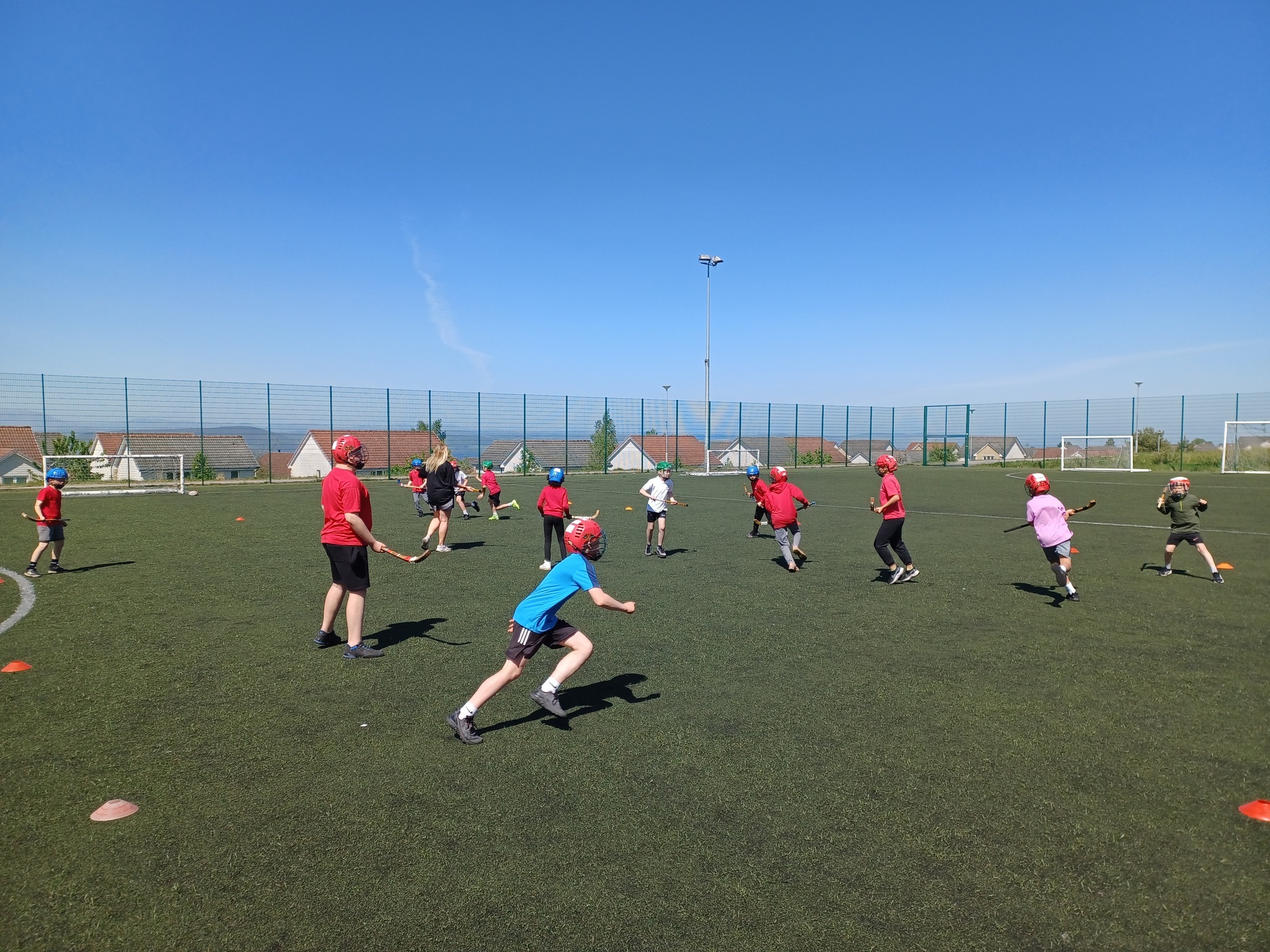 Children playing shinty on a pitch under a blue sky.