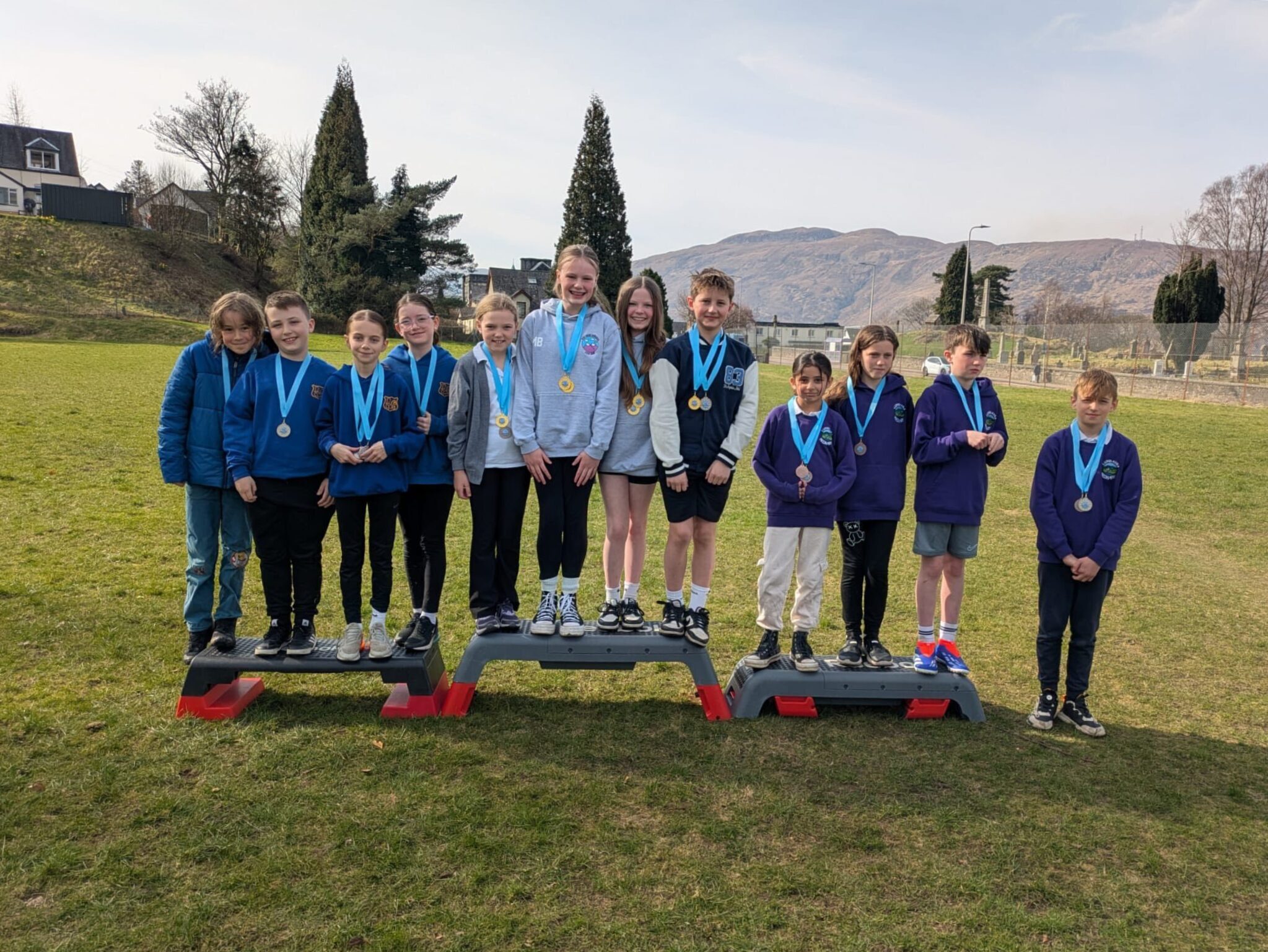 A group of smiling children standing on podium outside after Lochaber Swimming Gala 2025.