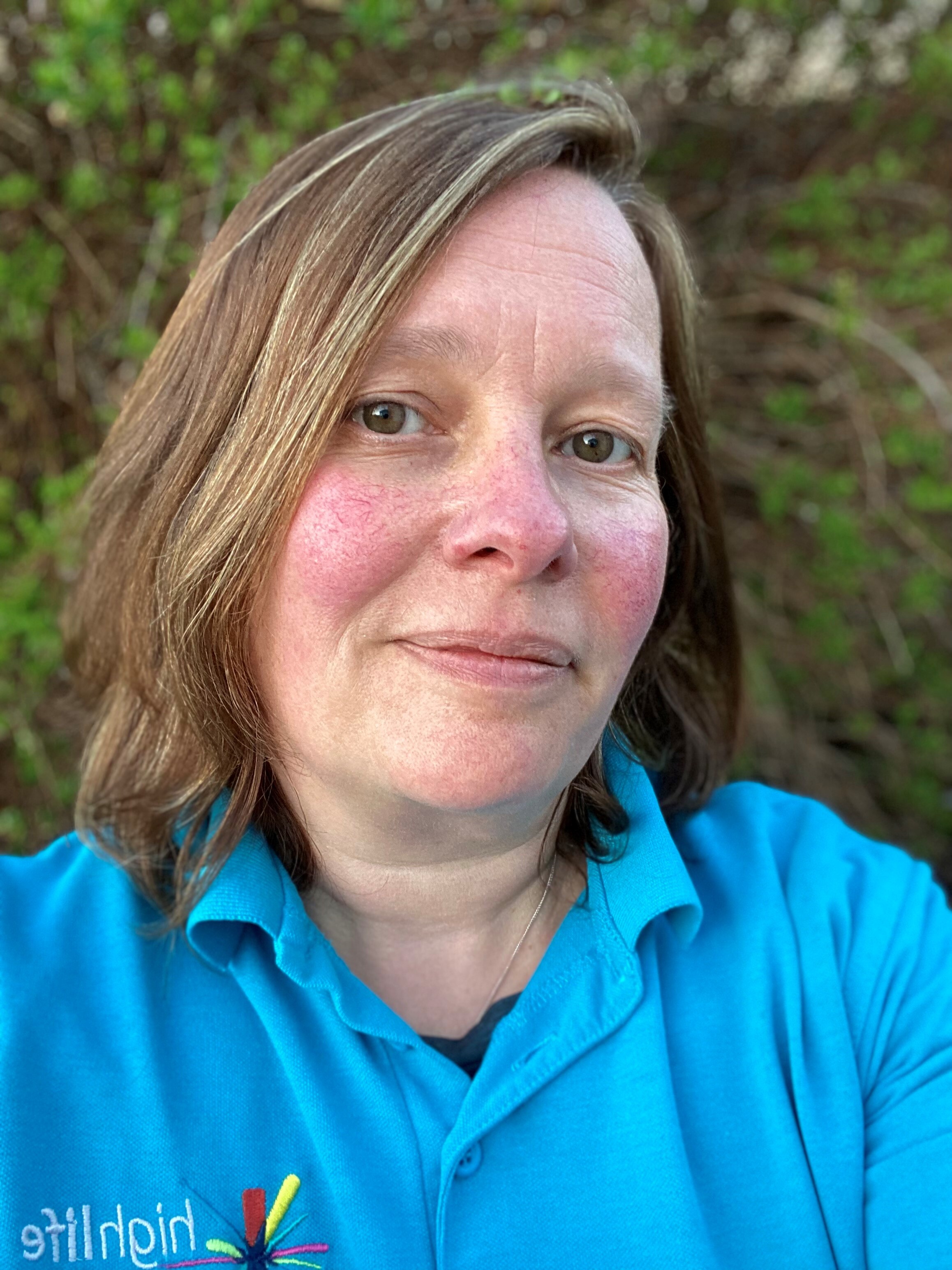 Countryside Ranger in a blue High Life Highland polo shirt outdoors with green foliage behind.