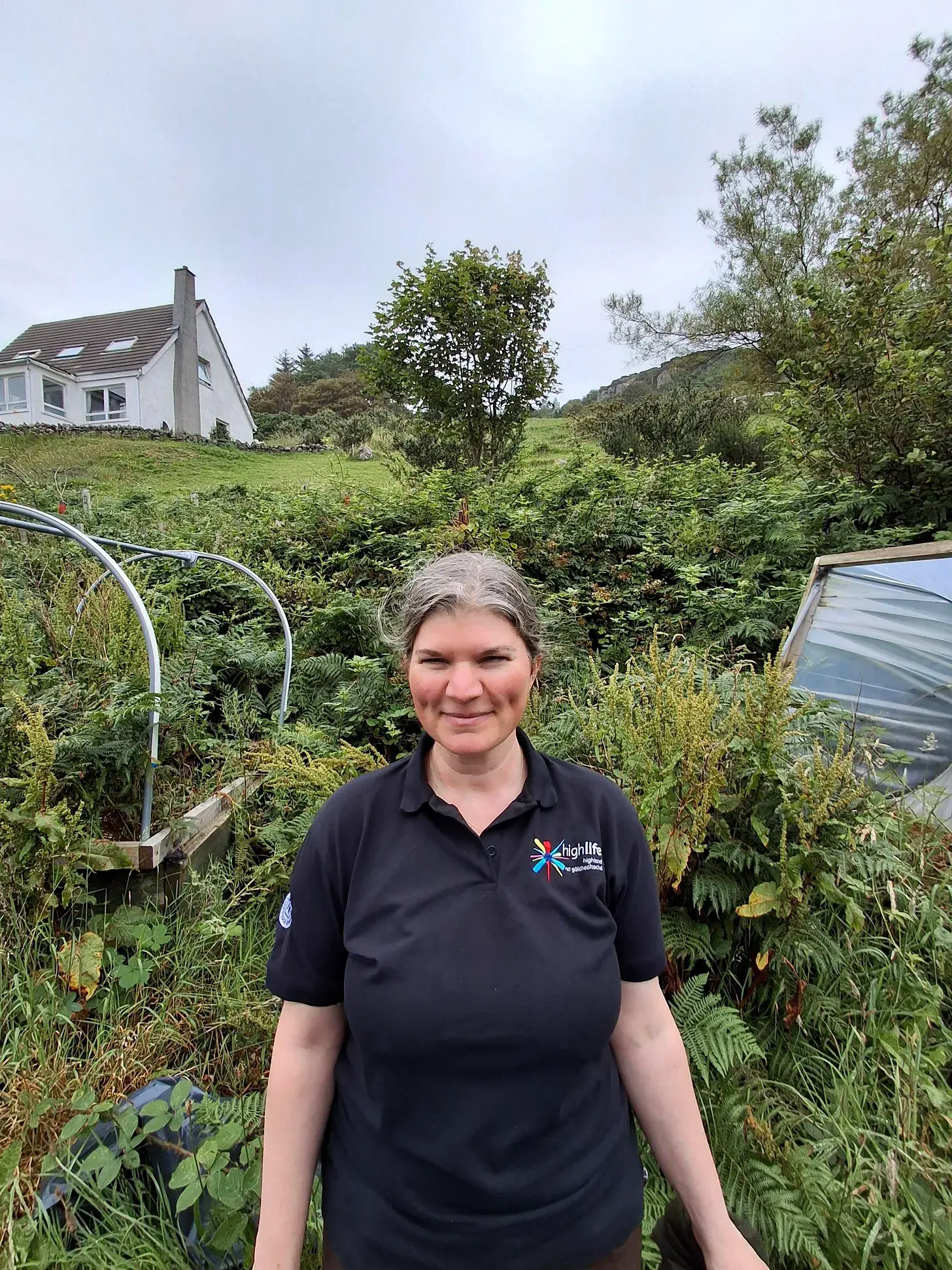 Countryside Ranger in a black High Life Highland polo shirt standing na garden area with a house in the background.