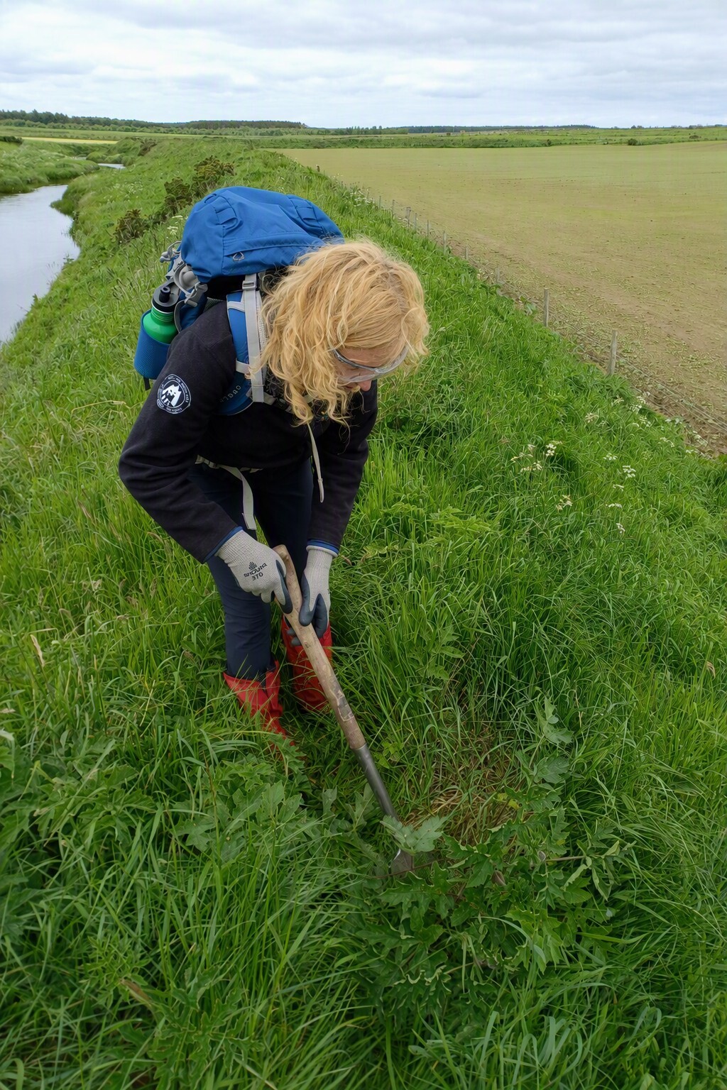 A female ranger in goggles and gloves digging in the ground