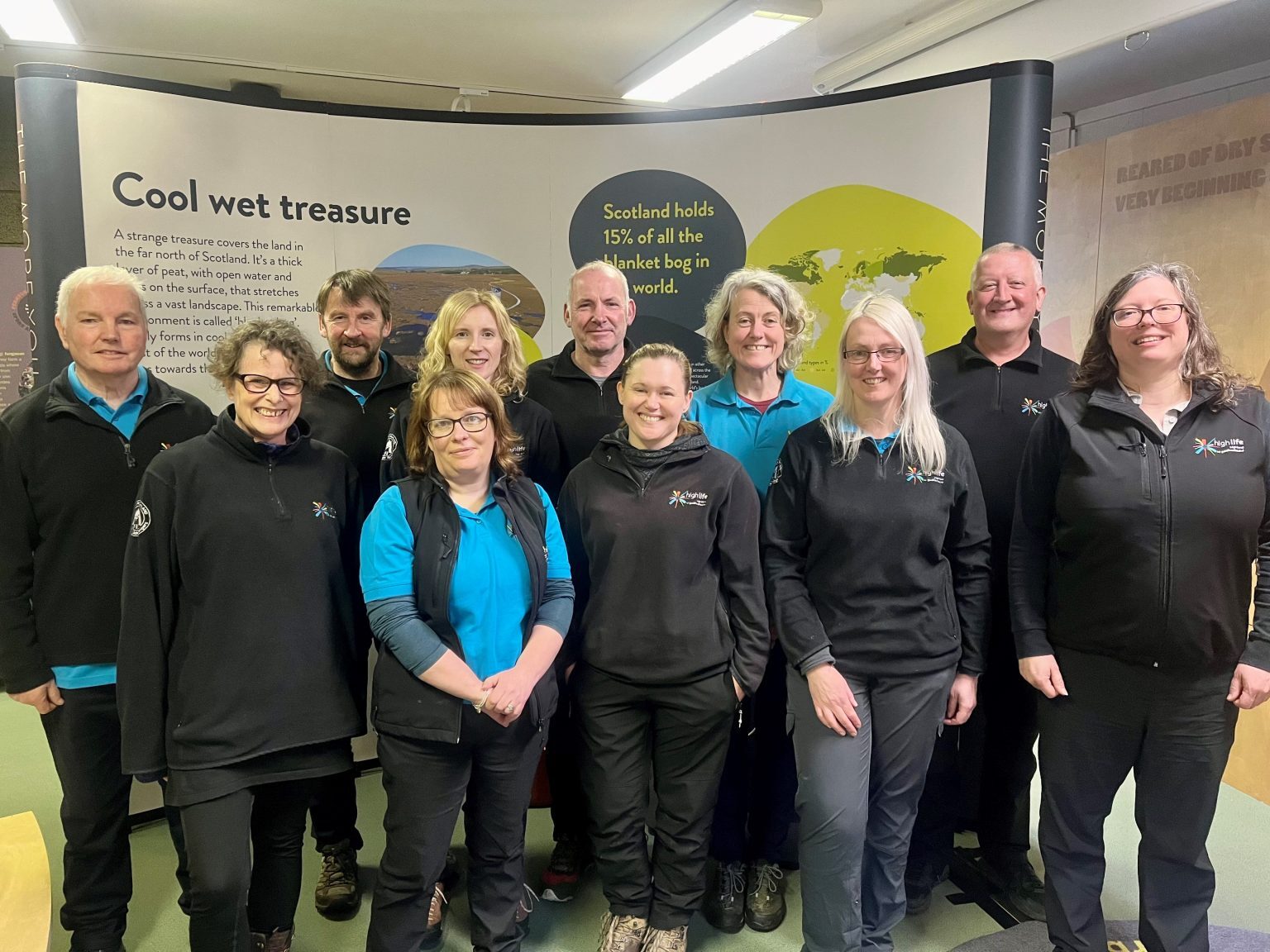 Group of Countryside Rangers standing indoors in front of an educational display about peat bogs and Scotland’s natural environment, wearing branded uniforms.