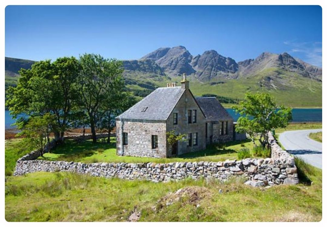 Traditional stone Torrin Bunkhouse on the Isle of Skye, surrounded by a stone wall with Loch Slapin and the Red Cuillin mountains in the background.