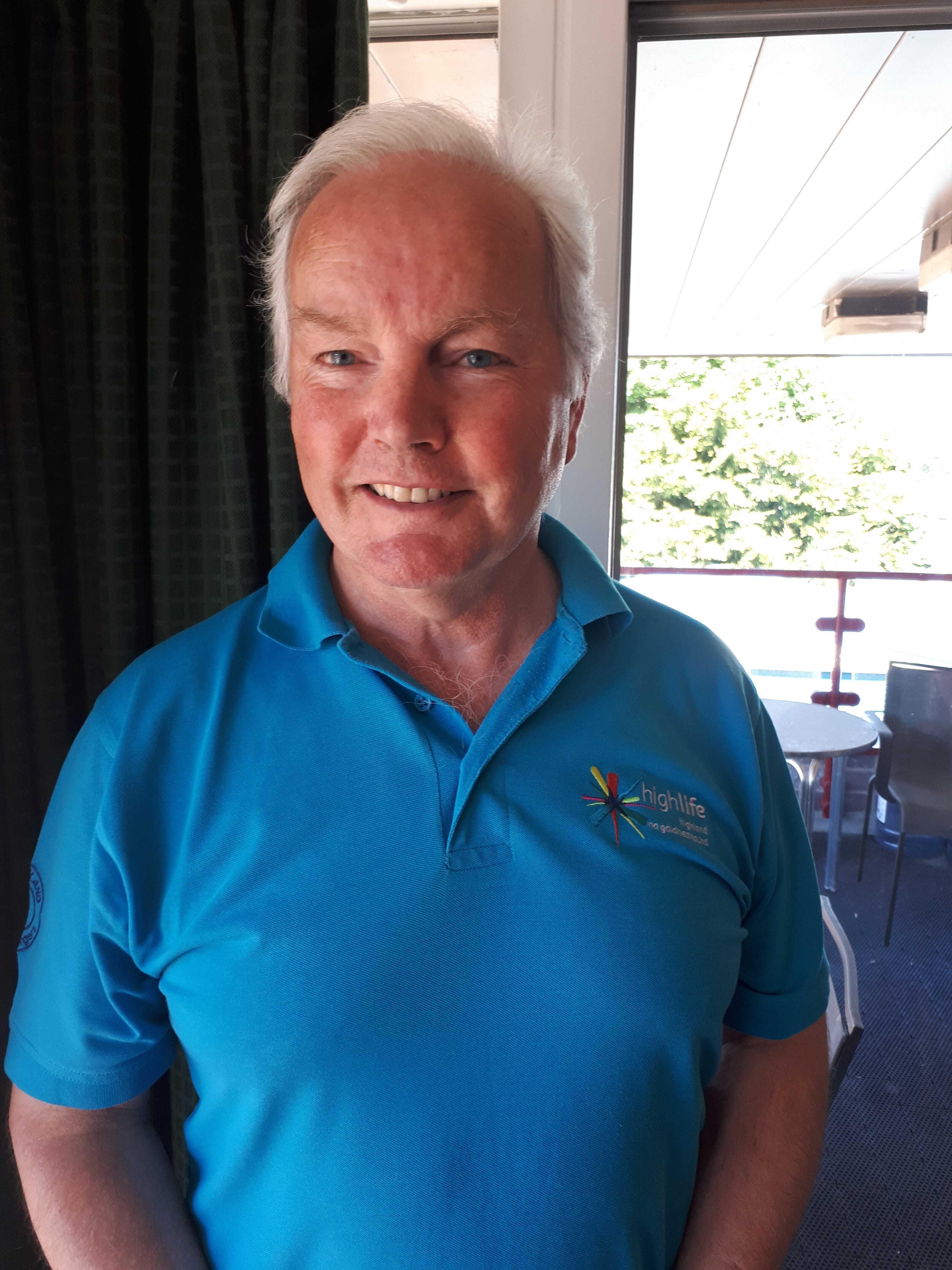 Countryside Ranger in a blue High Life Highland polo shirt standing indoors near a window with outdoor greenery visible.