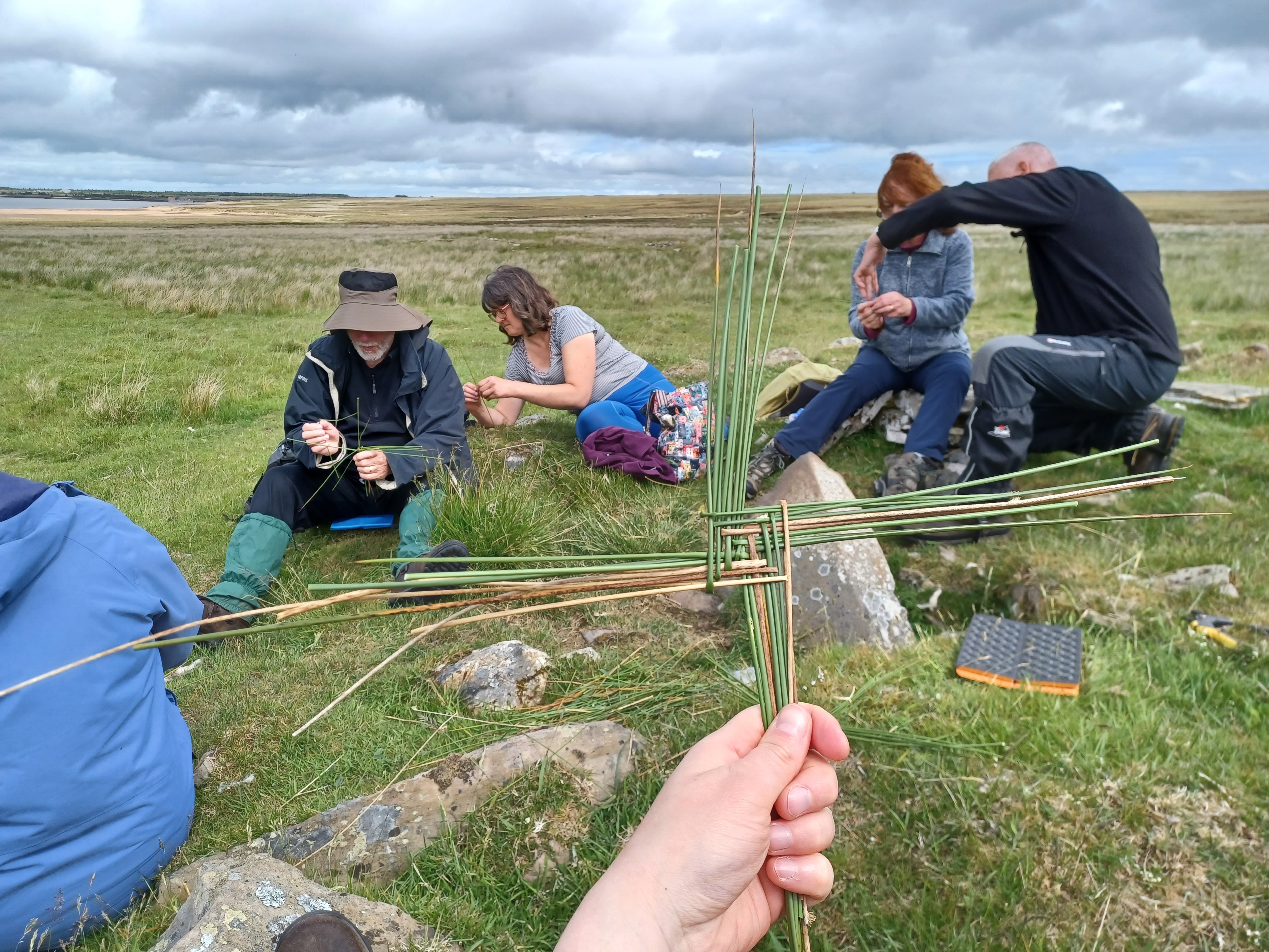 People undertaking a craft activity making crosses from rushes outside