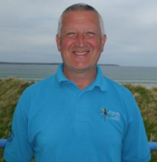 Countryside Ranger in a blue High Life Highland polo shirt standing near a coastal area with sea and dunes in the background.