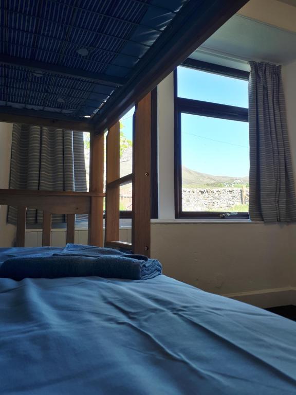 Bunk bed in a simple bunkhouse bedroom with blue bedding, folded towels, and a window overlooking stone walls and hills.