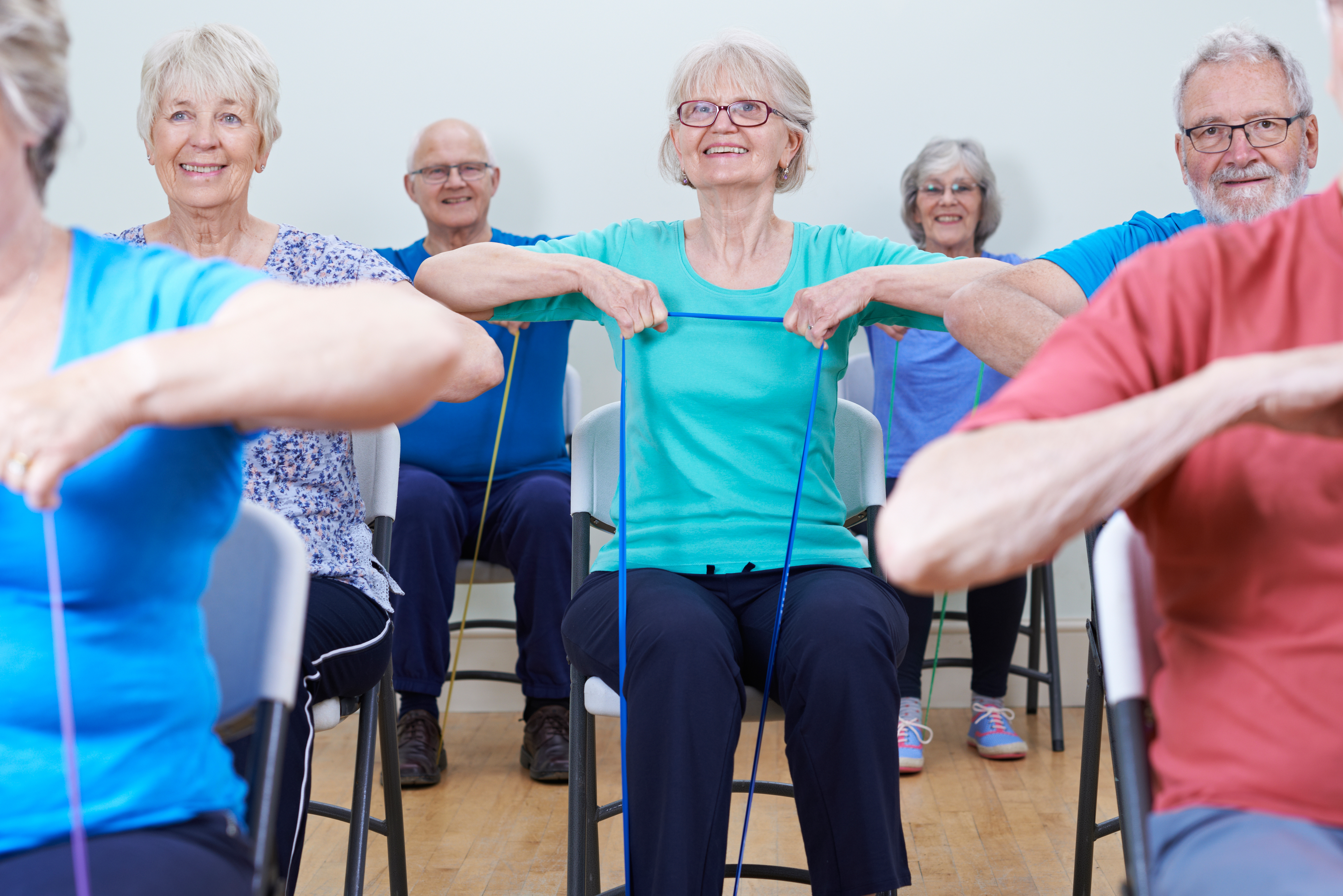 Group of people seated on chairs performing resistance band exercises in a fitness class setting.