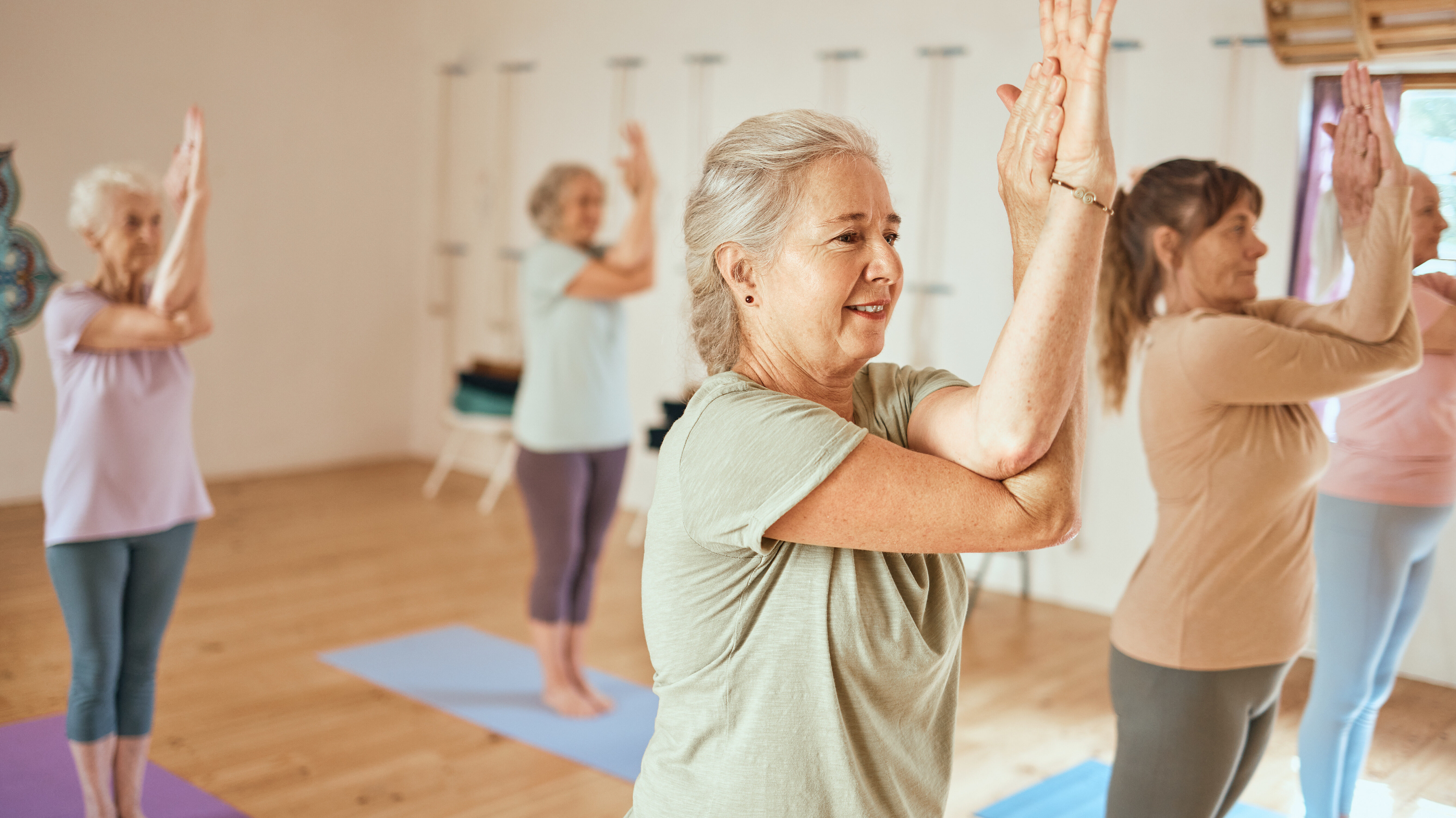 Group of people practicing yoga in a studio, standing on mats with arms crossed in an eagle pose.