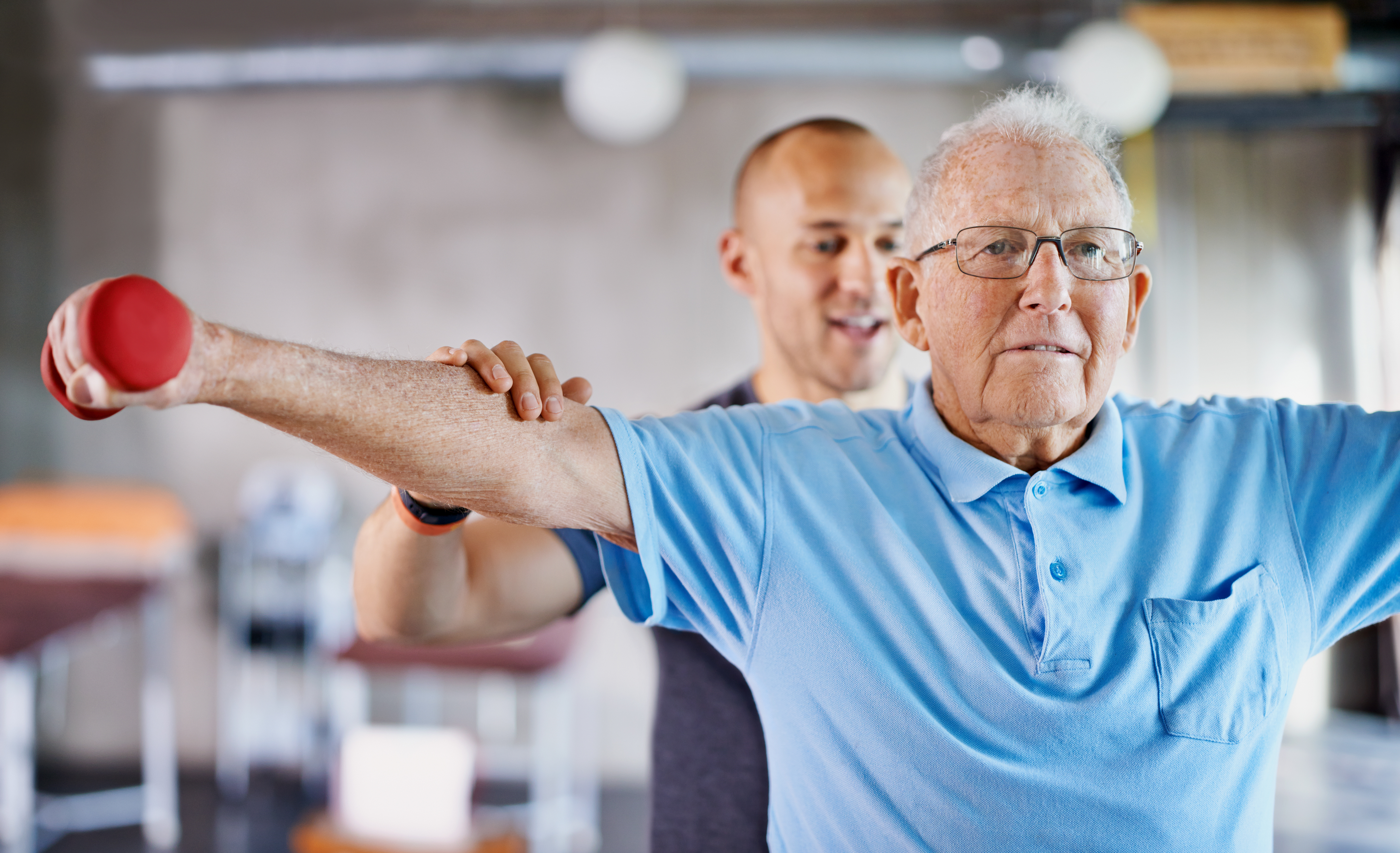 Instructor assisting an older adult with a lateral arm raise using a small dumbbell during exercise.