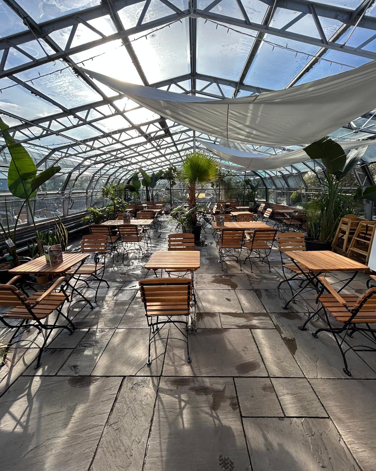 Sun shining into a glasshouse whilst sails provide some shading to tables and chairs.