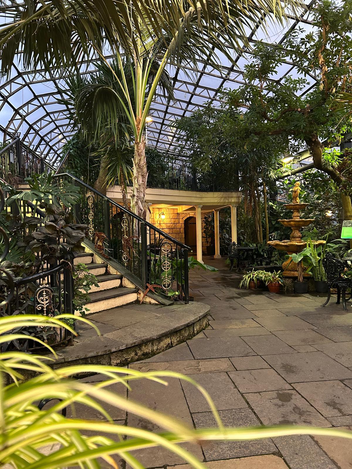 Interior of a tropical house with a staircase up to a mezzanine level, surrounded by tropical plants.