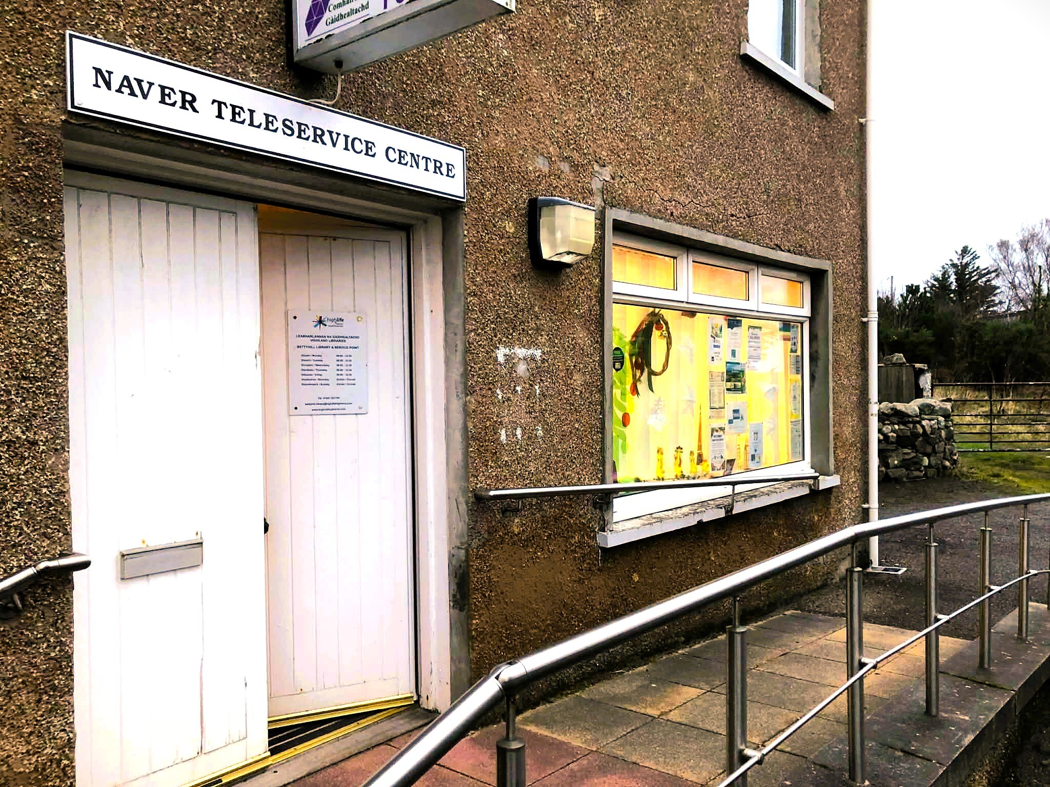 Exterior of Naver Teleservice Centre with a white door, sign above, and a bright window display, viewed from a ramped entrance.