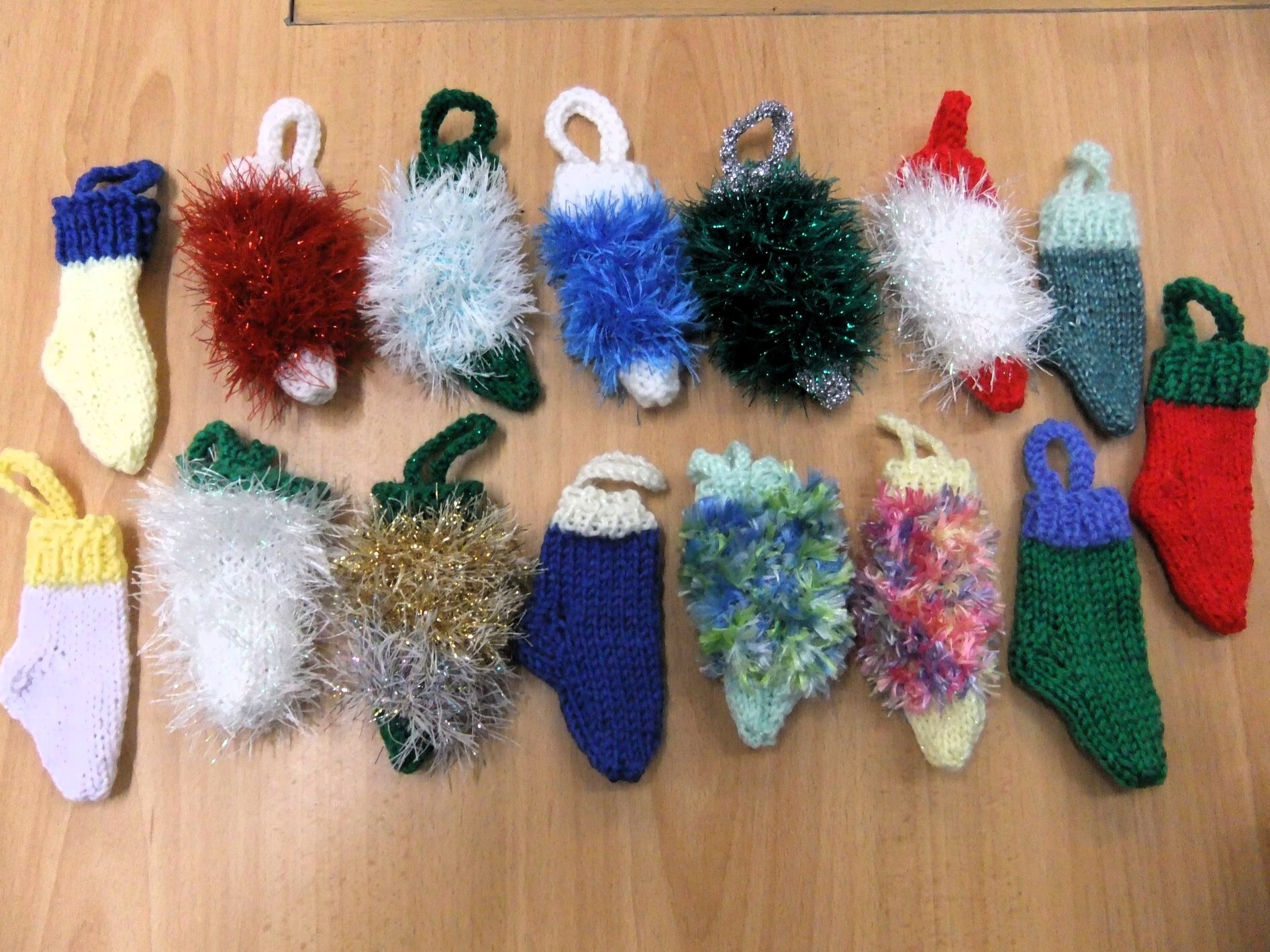 Sixteen small knitted Christmas stockings in bright colors and fluffy yarn, arranged in two rows on a wooden table.