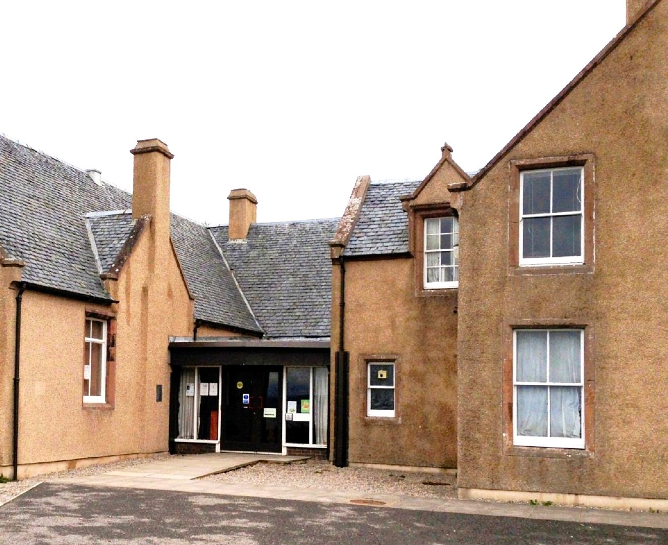 Traditional stone building with slate roof and chimneys, featuring a glass entrance in the center.