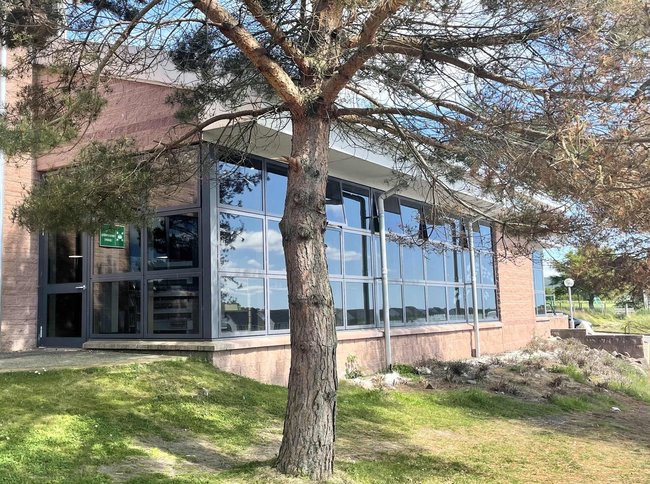 Exterior of Fortrose Library, modern building with large glass windows, surrounded by trees and greenery.