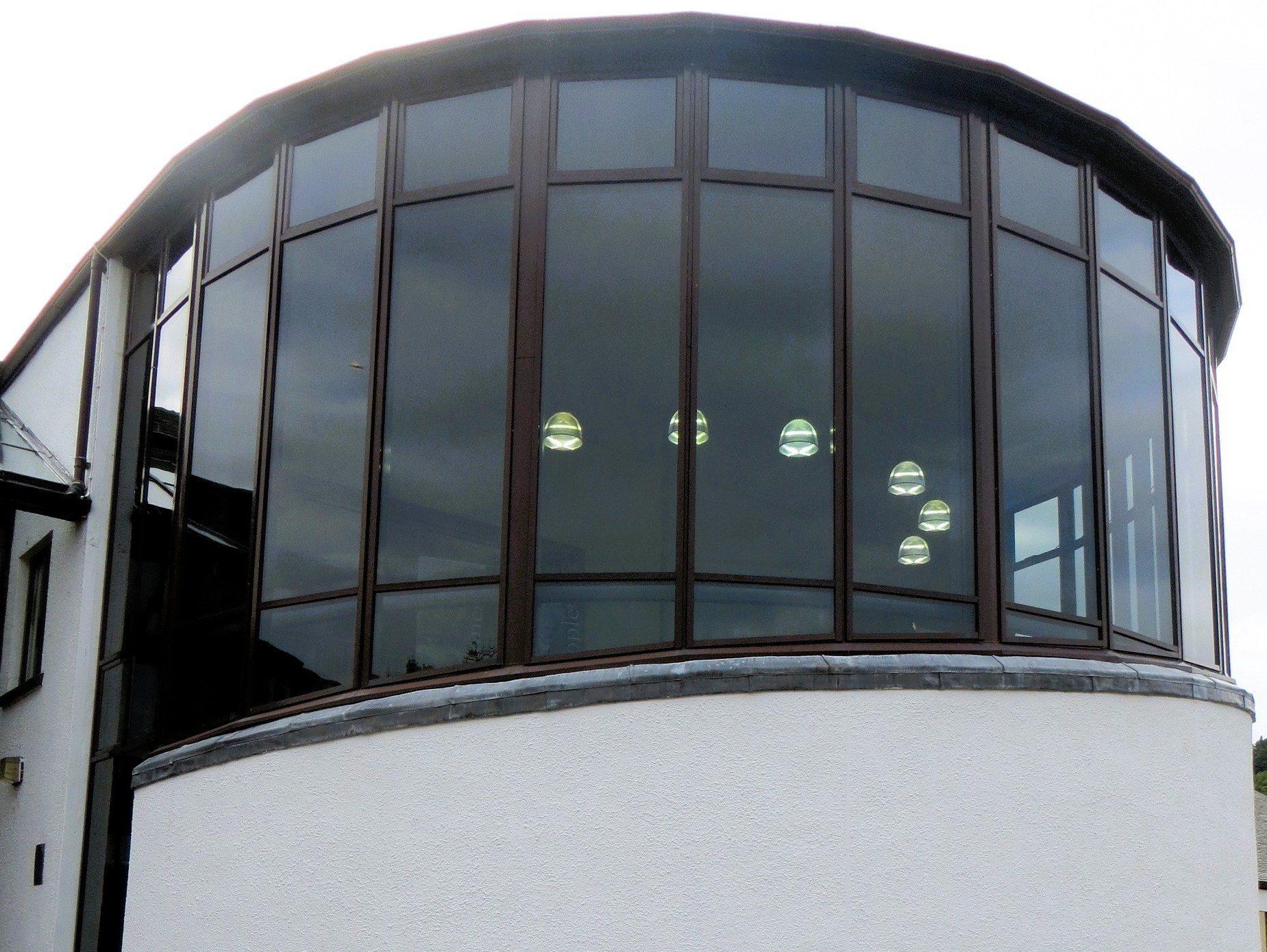 Curved glass-front section of Glenurquhart Library with large windows and visible hanging lights inside.
