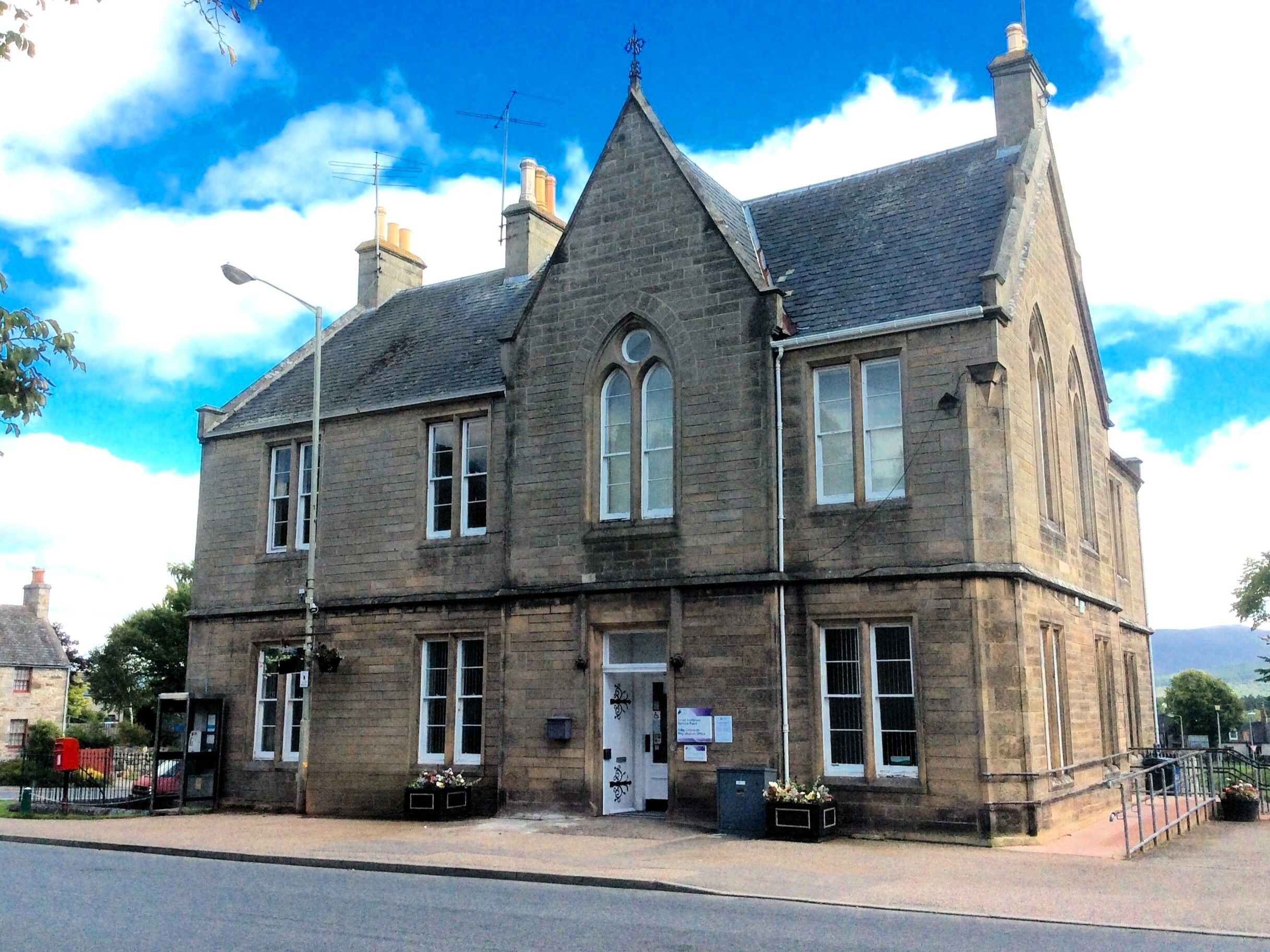 Front of Grantown Library, a large stone building with steep gabled roof, tall windows, and decorative chimneys.