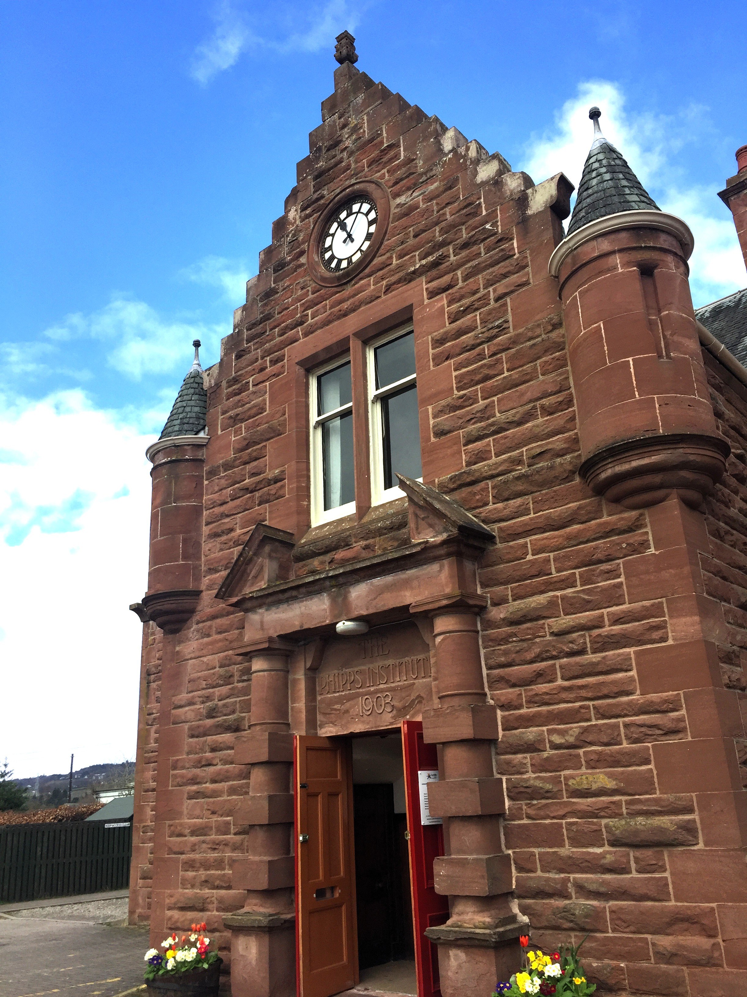Historic red sandstone building with a clock above the entrance and two conical turrets.