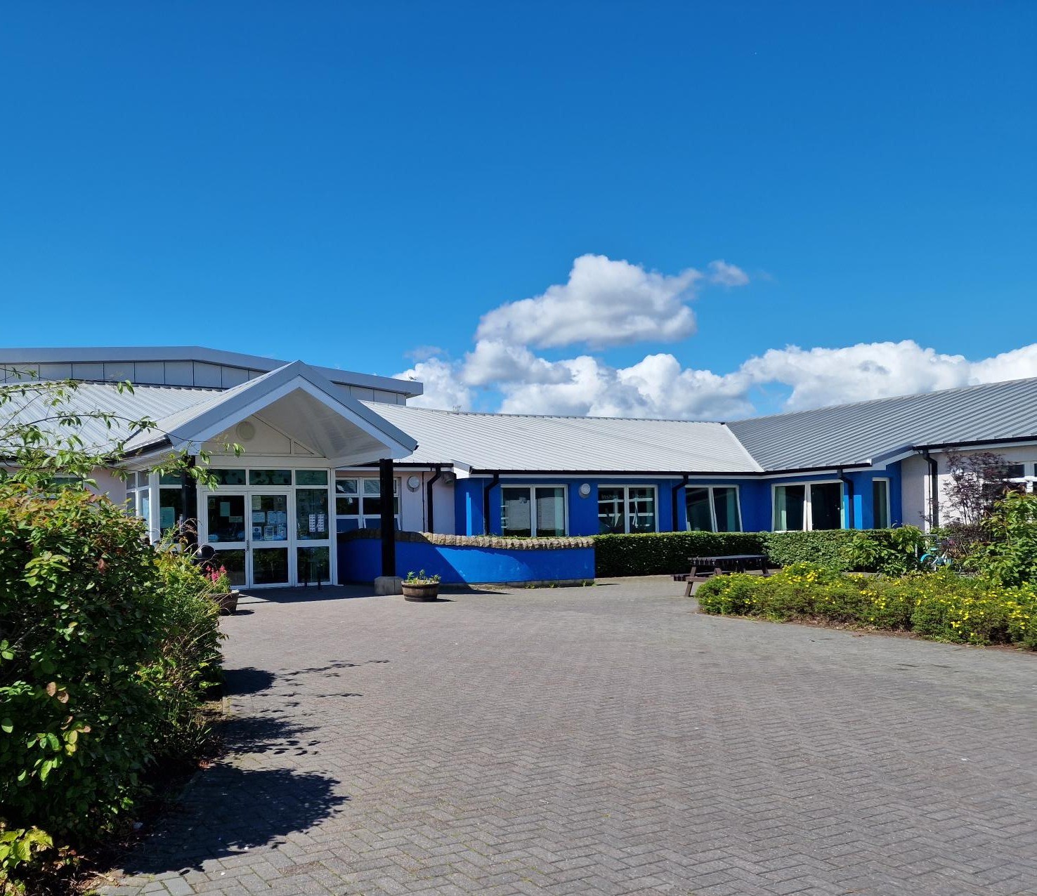 Front view of Inshes Library, a single-story blue building with a grey roof and a paved walkway leading to the entrance.