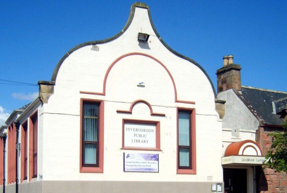 Front of Invergordon Library, white building with curved gable, red trim around windows, and bilingual signage.