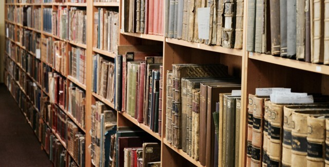 Rows of wooden bookshelves filled with old, worn books in various sizes and colors, creating a vintage library setting.